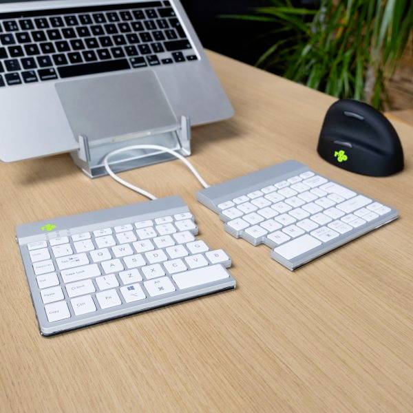 Na dřevěném stole stojí laptop se dvěma bezdrátovými klávesnicemi a myší. Laptop je umístěn na stojanu.
