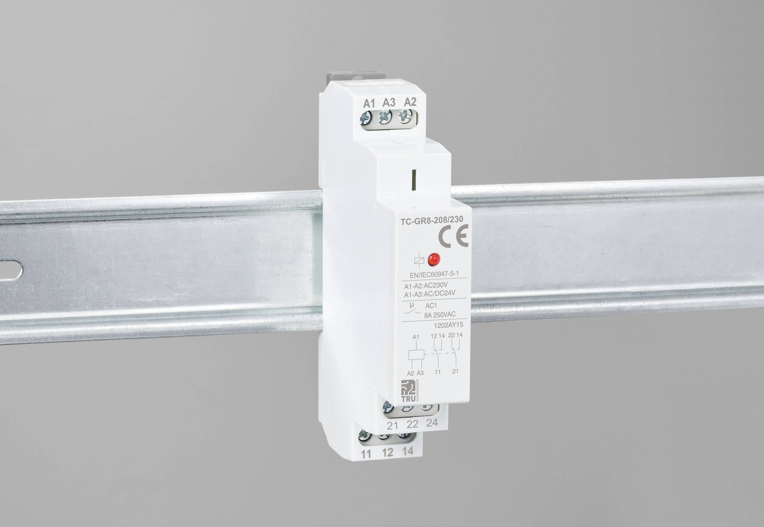 Elektrické relé je namontováno na kovovém pásu. Na přední straně ukazuje různé připojovací svorky a značku CE.
