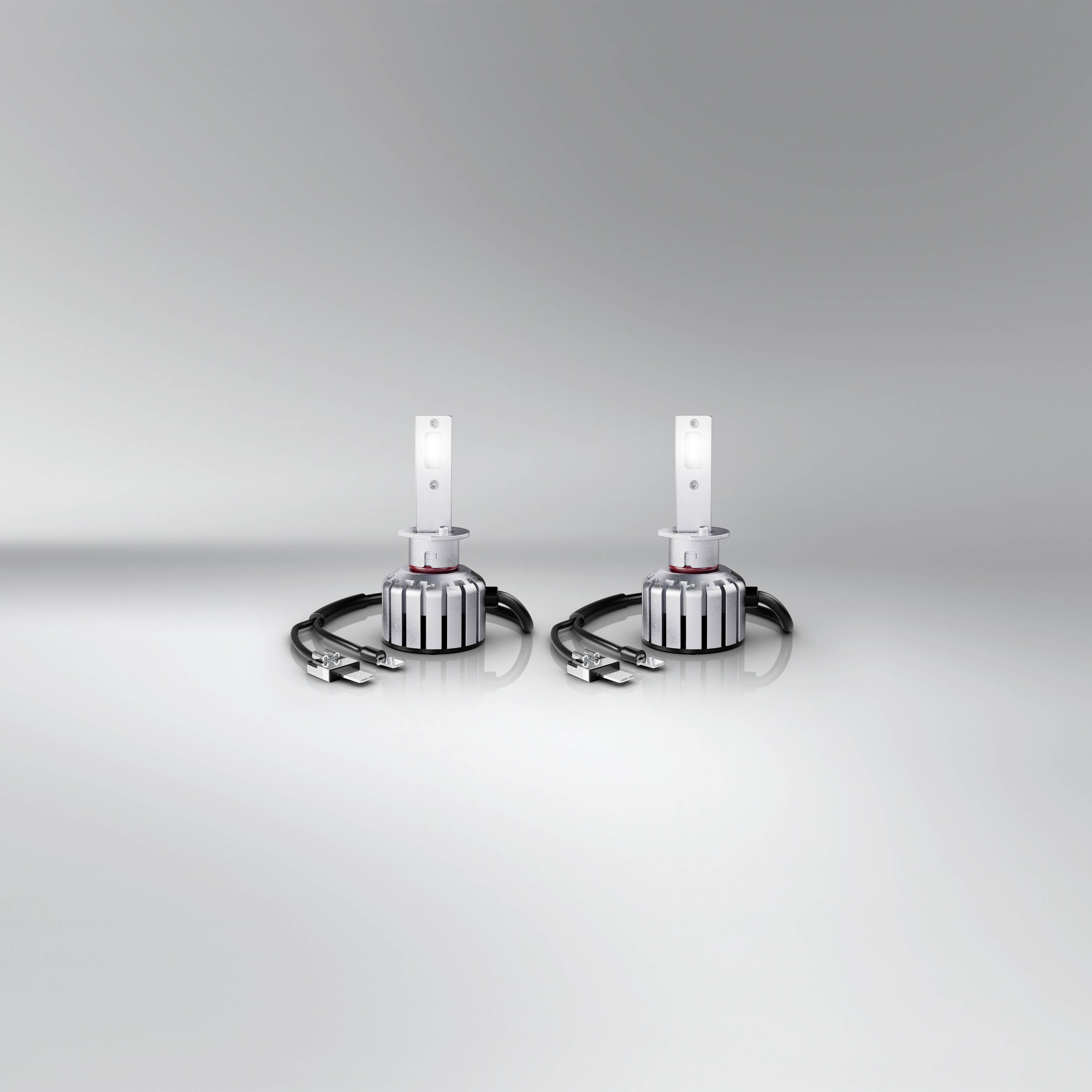 Dvě identické LED lampy s chladiči a kabely, uspořádané na šedém povrchu. Působí moderně a technicky.
