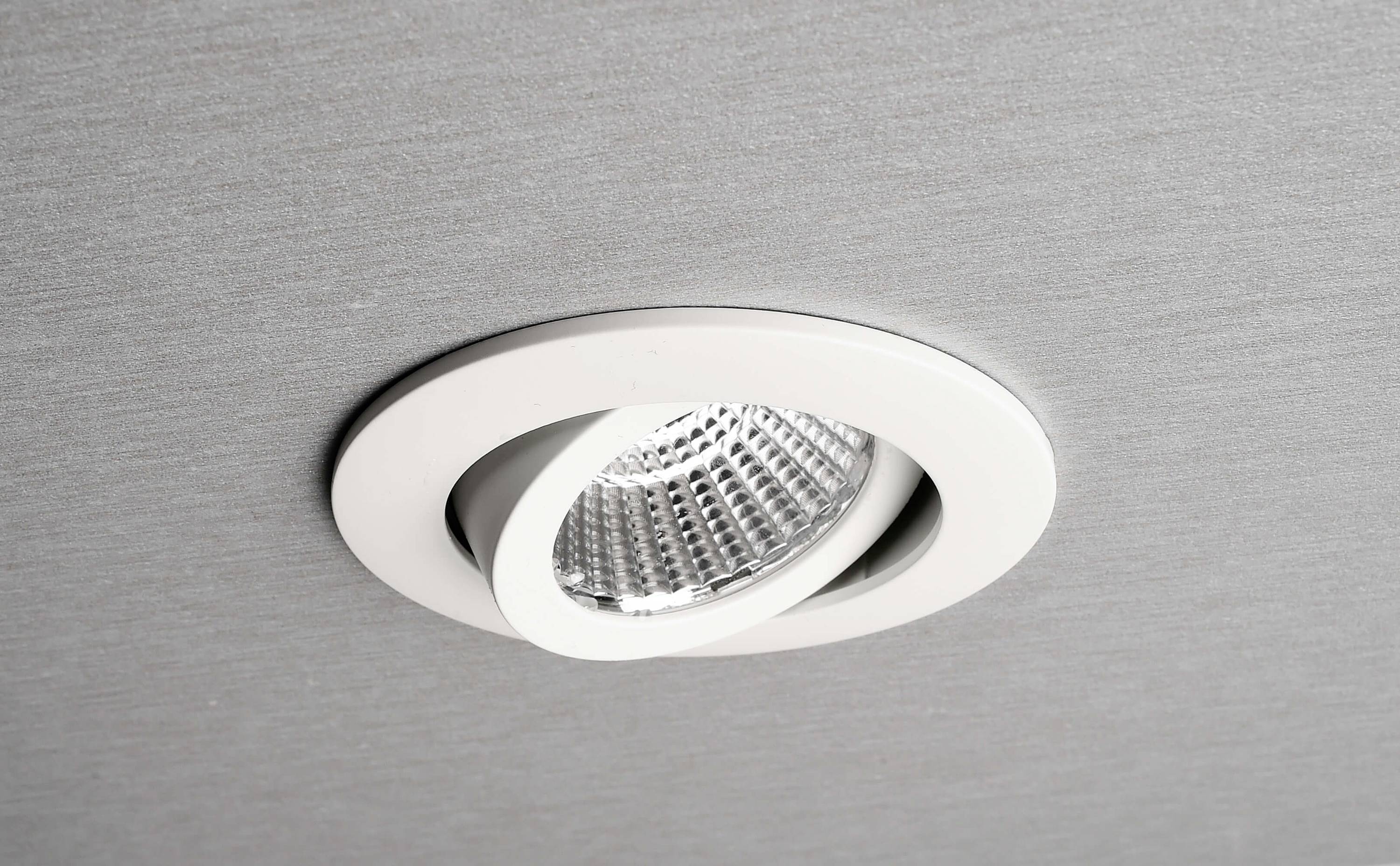 Vestavěné svítidlo namontované v podhledu ukazuje moderní, minimalistický design s bílým rámečkem a stříbrným vnitřním reflektorem.