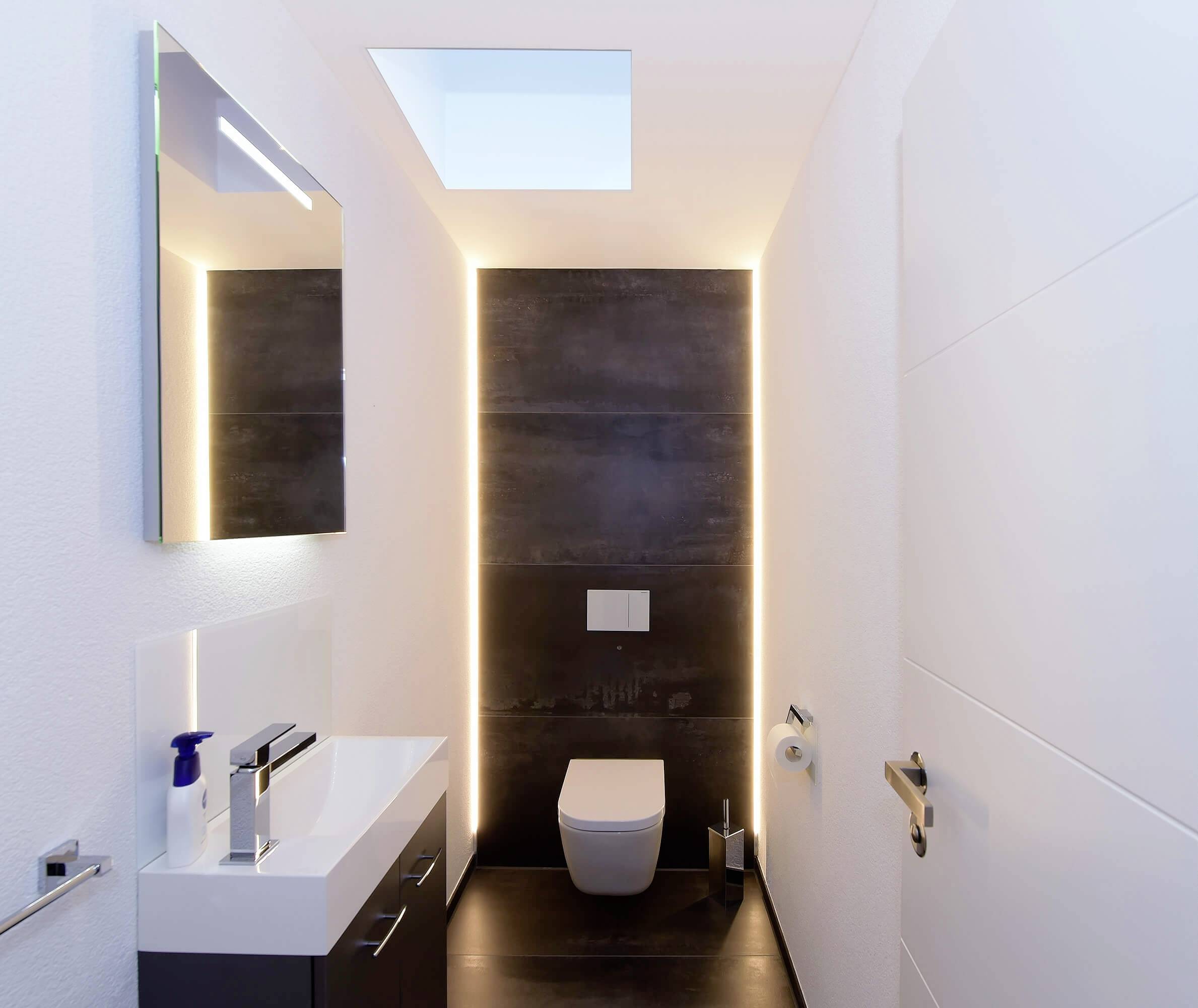 Moderní koupelna s minimalistickým designem, toaletou a umyvadlem. Osvětlení a barvy vytvářejí elegantní atmosféru.