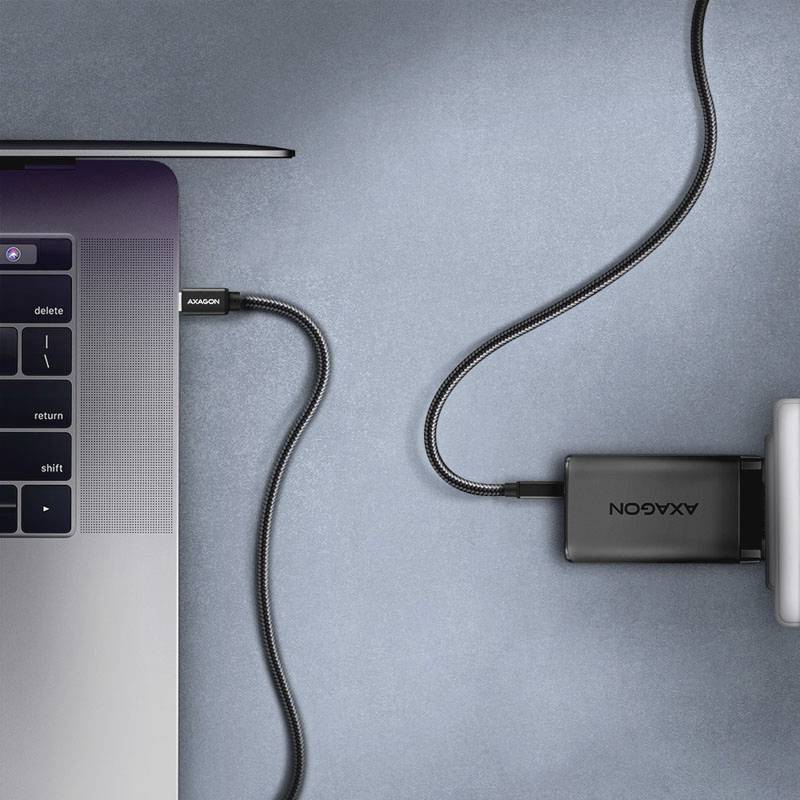 Notebook je připojeno k externímu nabíječi pomocí kabelu USB-C. Nabíječ leží vpravo vedle notebooku.