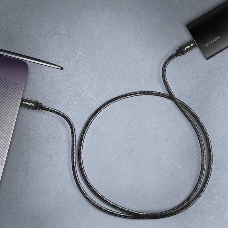 USB-C kabel propojuje laptop s externím zařízením. Obě zařízení jsou zčásti viditelná. Na kabelu je nápis „AXAGON".