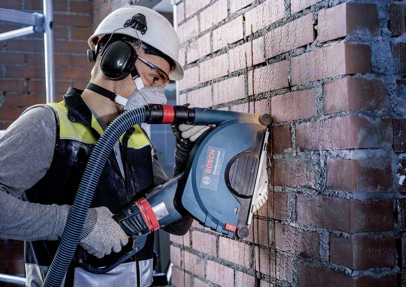 Dělník v ochranném oblečení používá elektrický nástroj k řezání cihlové zdi.