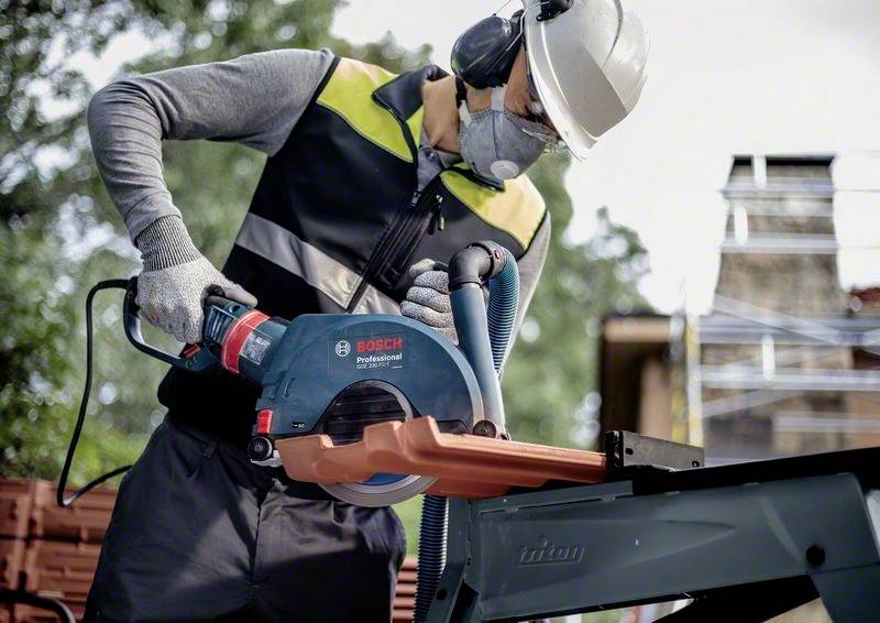 Osoba v ochranných brýlích a helmě řeže kotoučovou pilou Bosch kus kovu venku. Bezpečnost je na prvním místě.