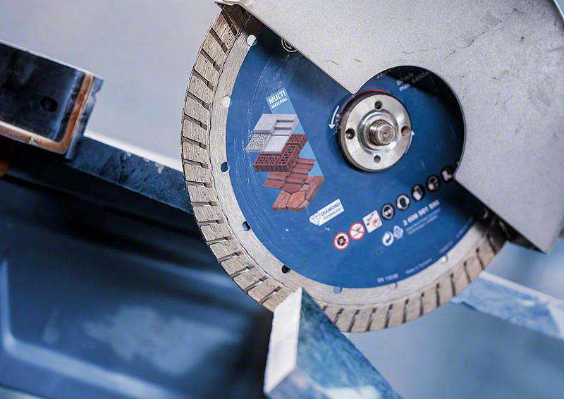 Úhlová bruska s diamantovým řezným kotoučem řeže kov. Kotouč je vhodný pro beton a cihly. Bezpečnostní označení jsou viditelná.