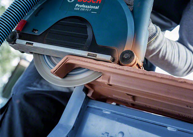 Osoba řeže střešní tašku elektrickou pilou značky Bosch. Důraz je kladen na samotný řezací proces a použitý nástroj.