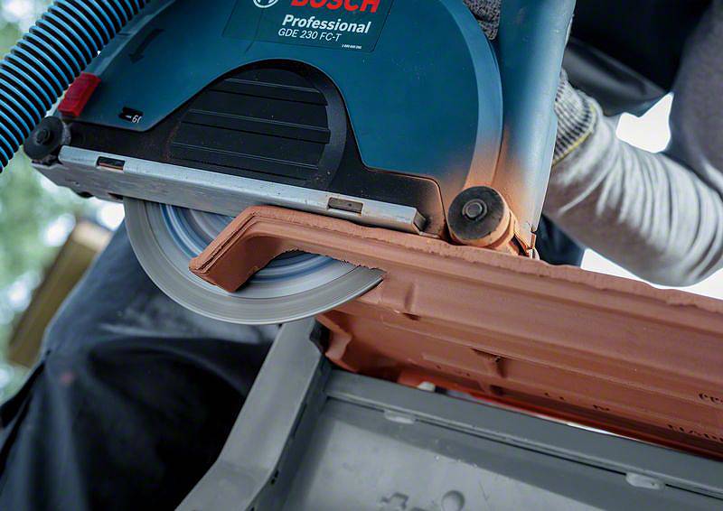 Osoba používá elektrickou pilu k řezání střešní tašky. Pila je označena štítkem 'Bosch Professional'.