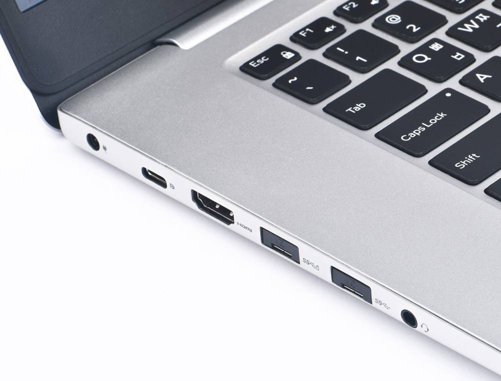 Detailní záběr notebooku s různými porty, včetně HDMI, USB a sluchátkového vstupu, které umožňují komunikaci a připojení.