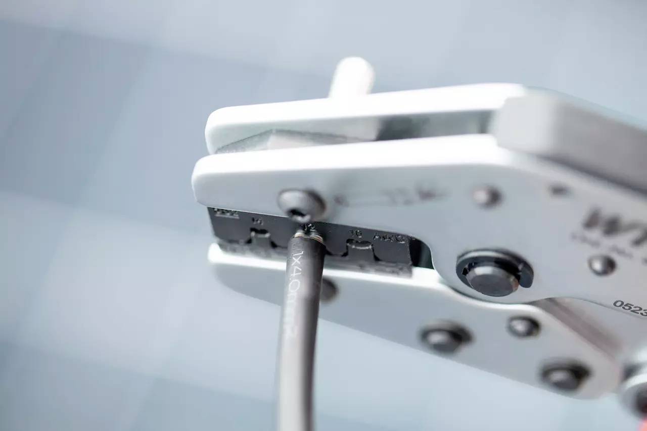 Detailní záběr kleští na krimpování, která zpracovává kabel. Scéna zdůrazňuje přesnost a funkčnost nástroje.