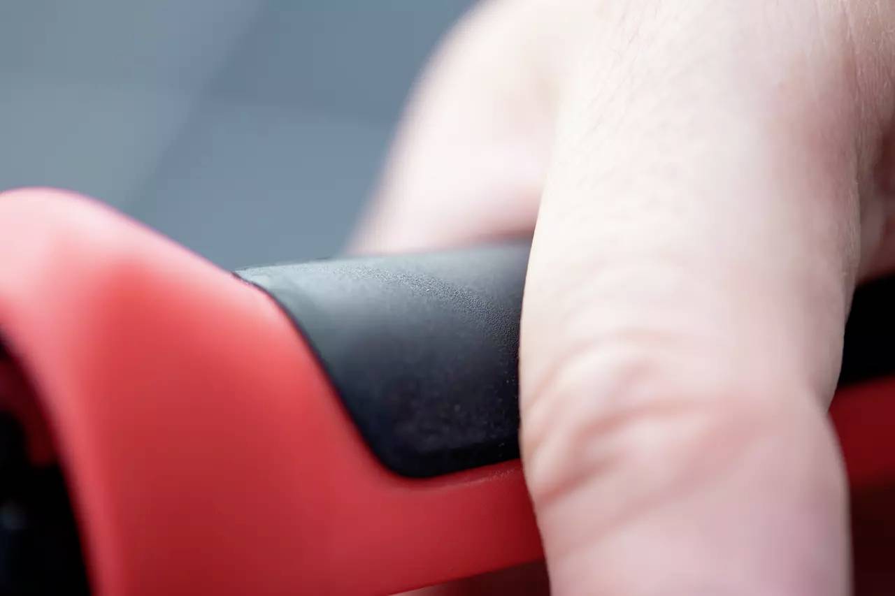 Detailní záběr prstu svírajícího červeno-černou rukověť.