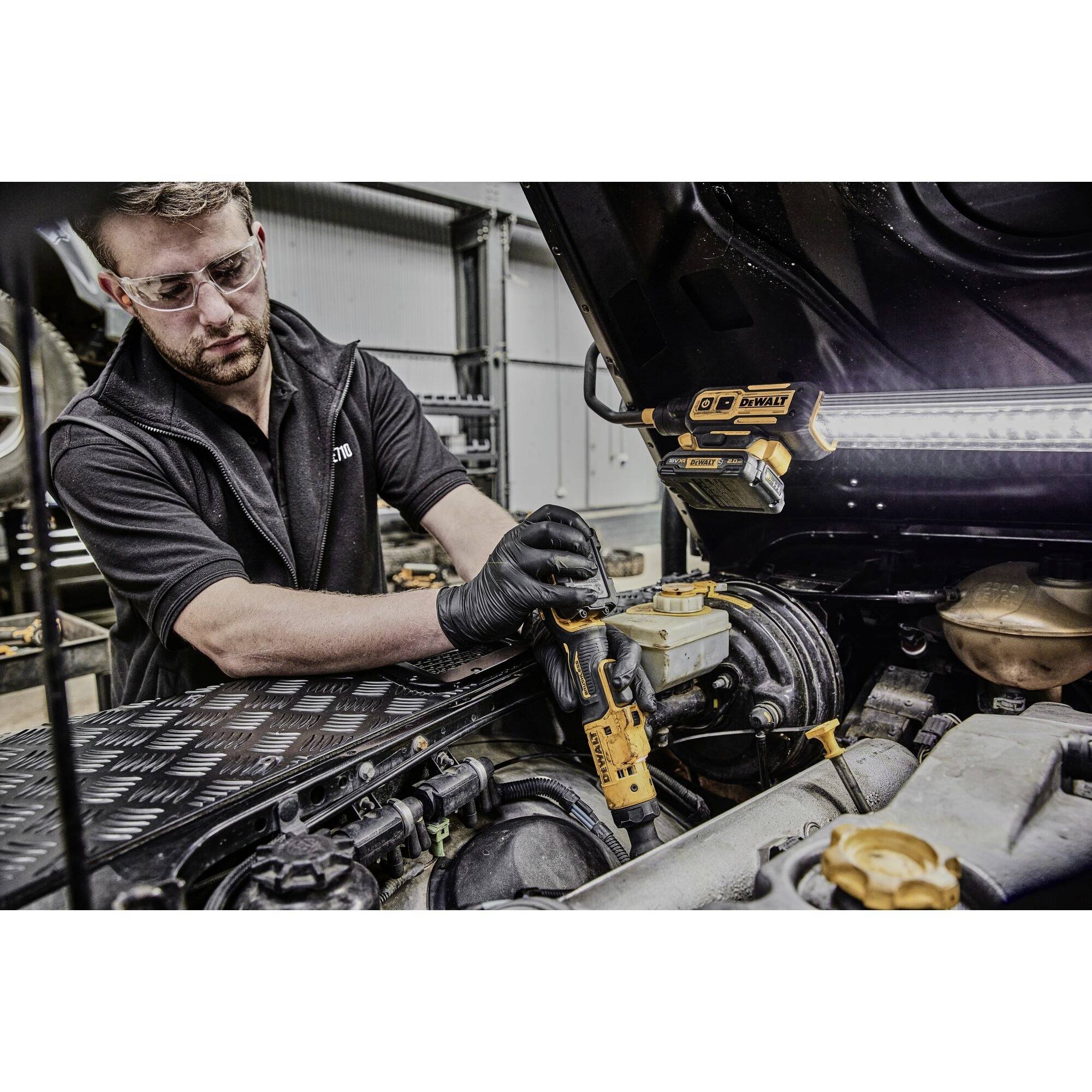 Muž v pracovním oblečení opravuje vnitřek otevřeného kufru automobilu pomocí šroubováku. Je vybaven bezpečnostními brýlemi a má zajištěno osvětlení.