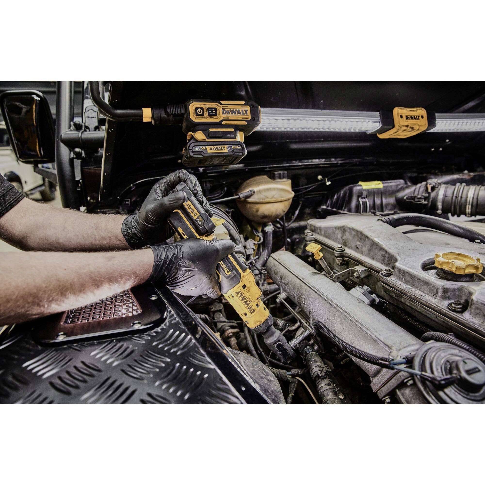 Mechanik používá elektrický nástroj při práci na automobilu. Motorový prostor je otevřený a viditelný.