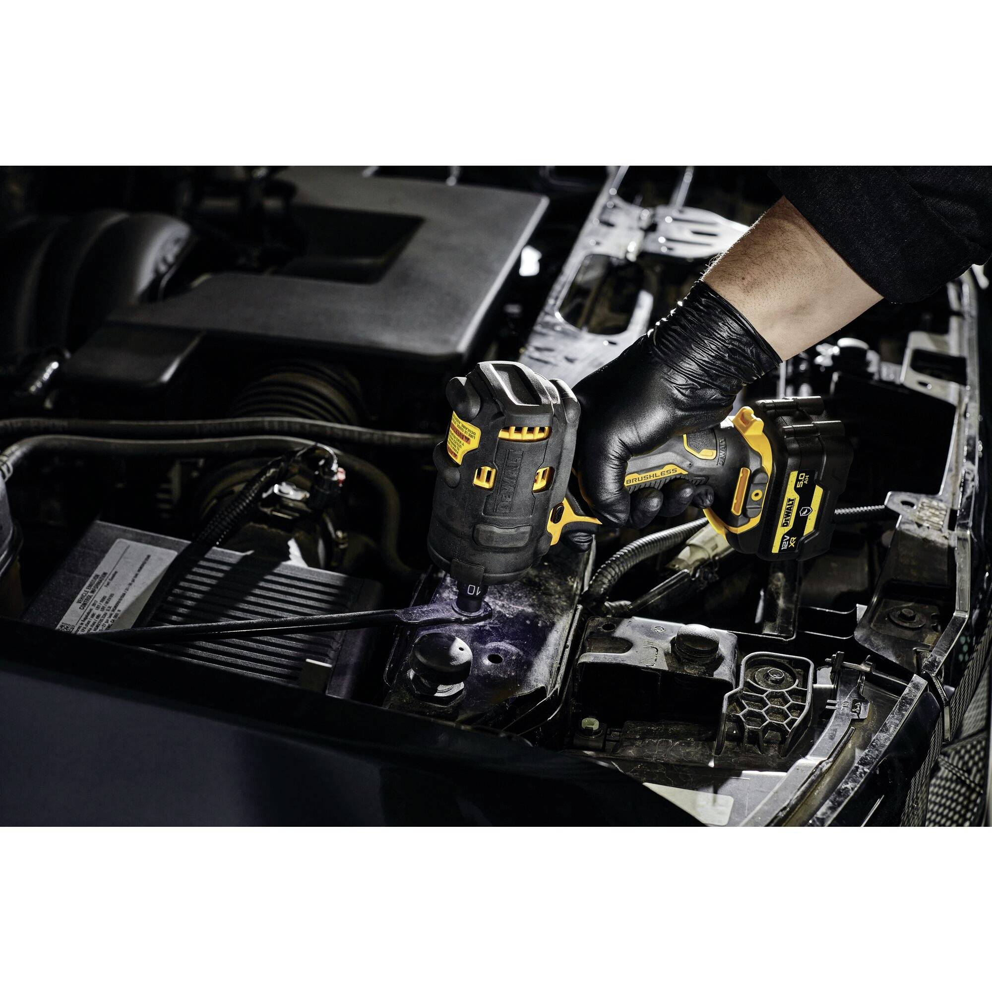 Mechanik používá akumulátorový rázový utahovák při práci na automobilovém motoru. Motorový prostor je částečně viditelný.