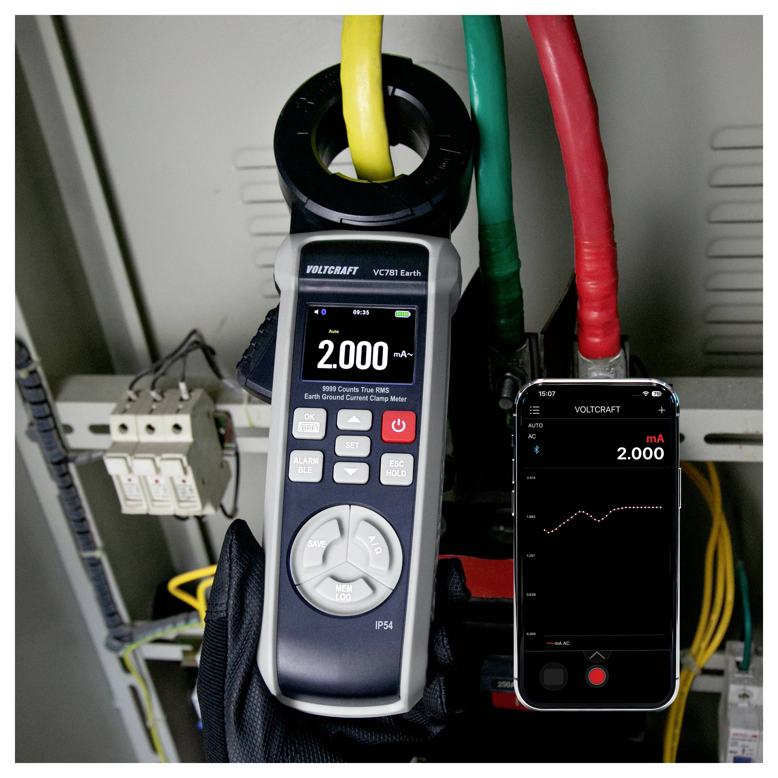 Kleštový ampérmetr měřící 2.000 mA na velkém žlutém kabelu uvnitř elektrického panelu, s aplikací v telefonu zrcadlící údaj.