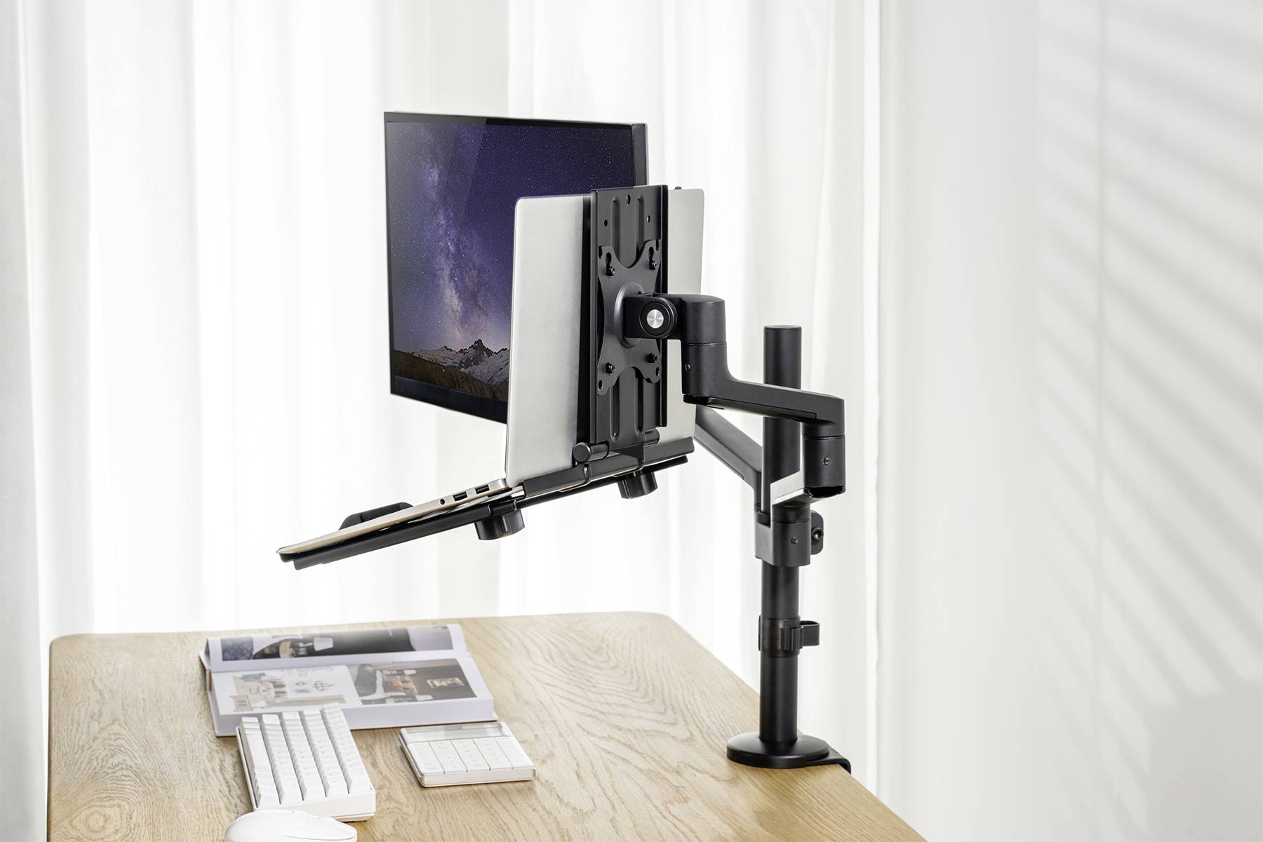Notebook a monitor jsou upevněny na nastavitelném rameni pro dva monitory. Nachází se na dřevěném stole vedle klávesnice a myši.