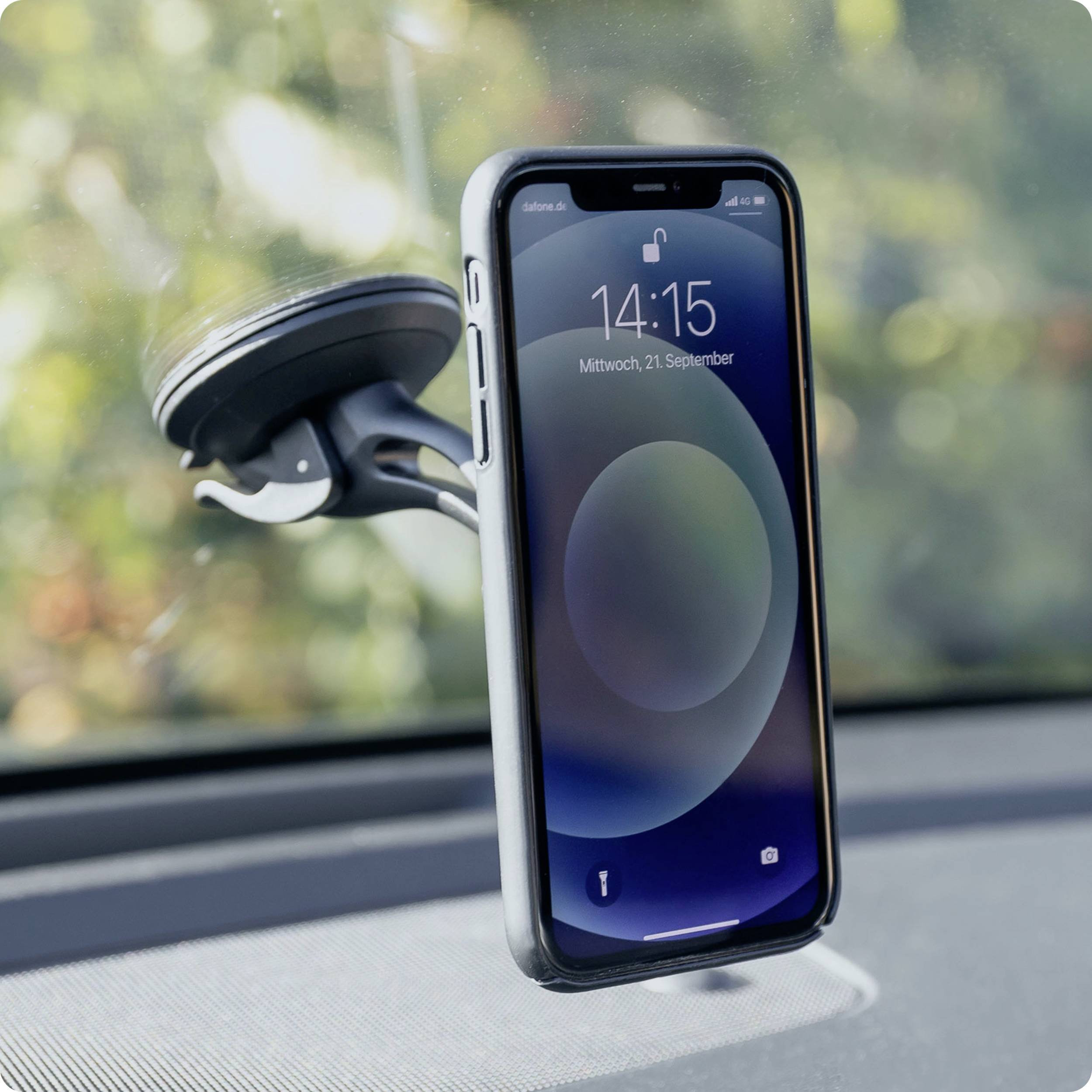 Smartphone v černém obalu je upevněno v držáku na čelním skle automobilu. Na displeji je zobrazeno 14:15.