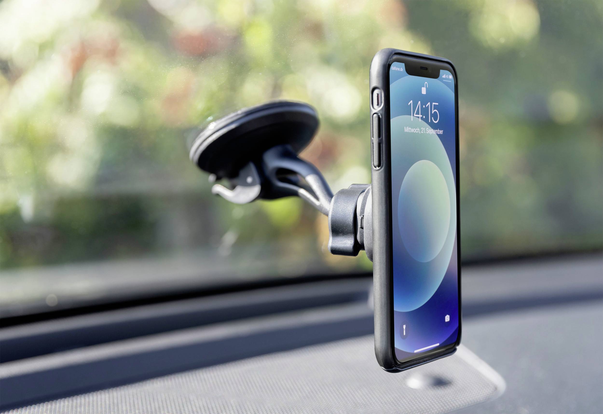 Smartphone v držáku na čelním skle automobilu, v pozadí rozmazané stromy.