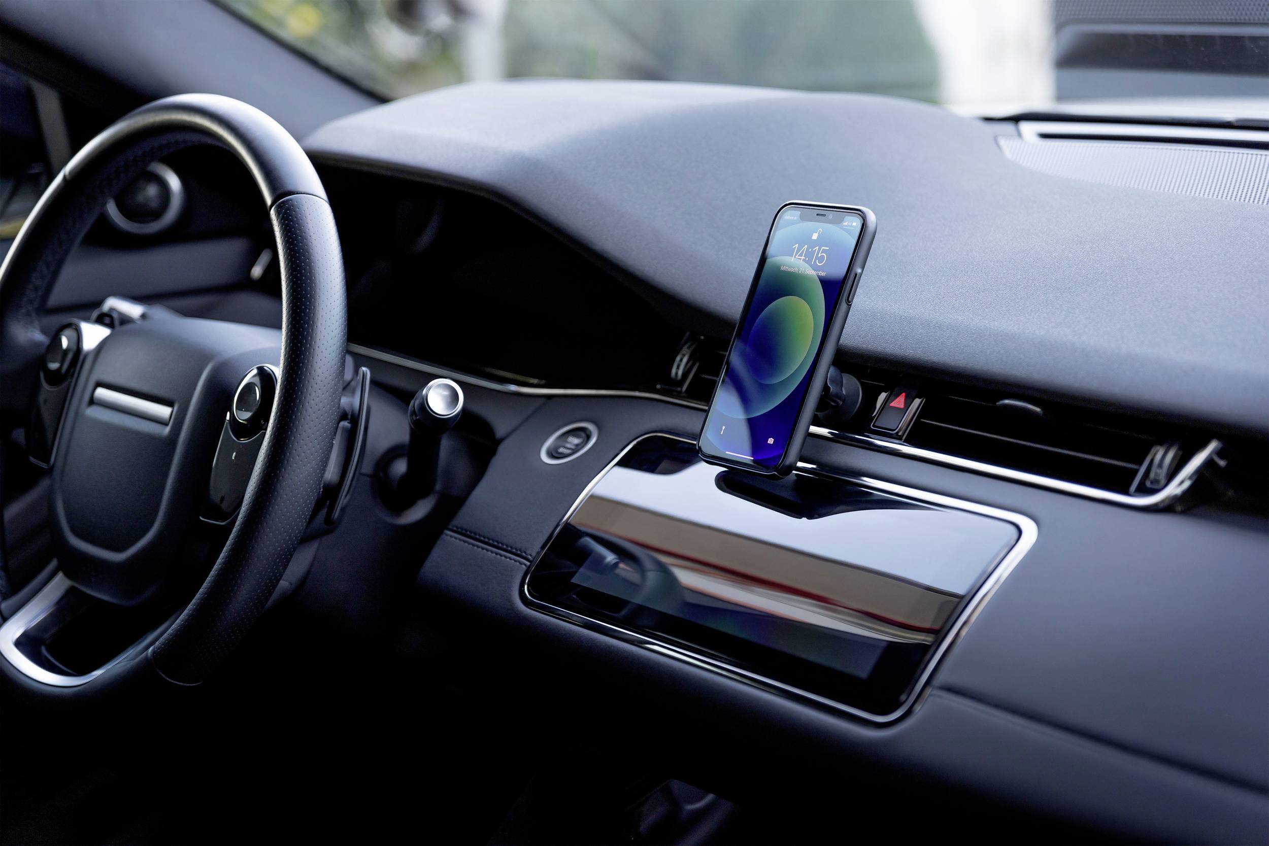 Smartphone s modrou obálkou je vzpřímeně umístěno na palubní desce vozu. Displej zobrazuje čas.
