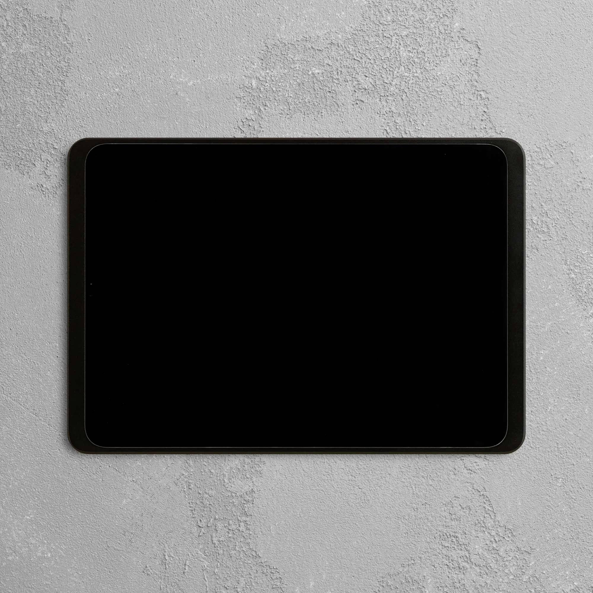 Černý tablet s vypnutou obrazovkou leží na šedém strukturovaném povrchu.