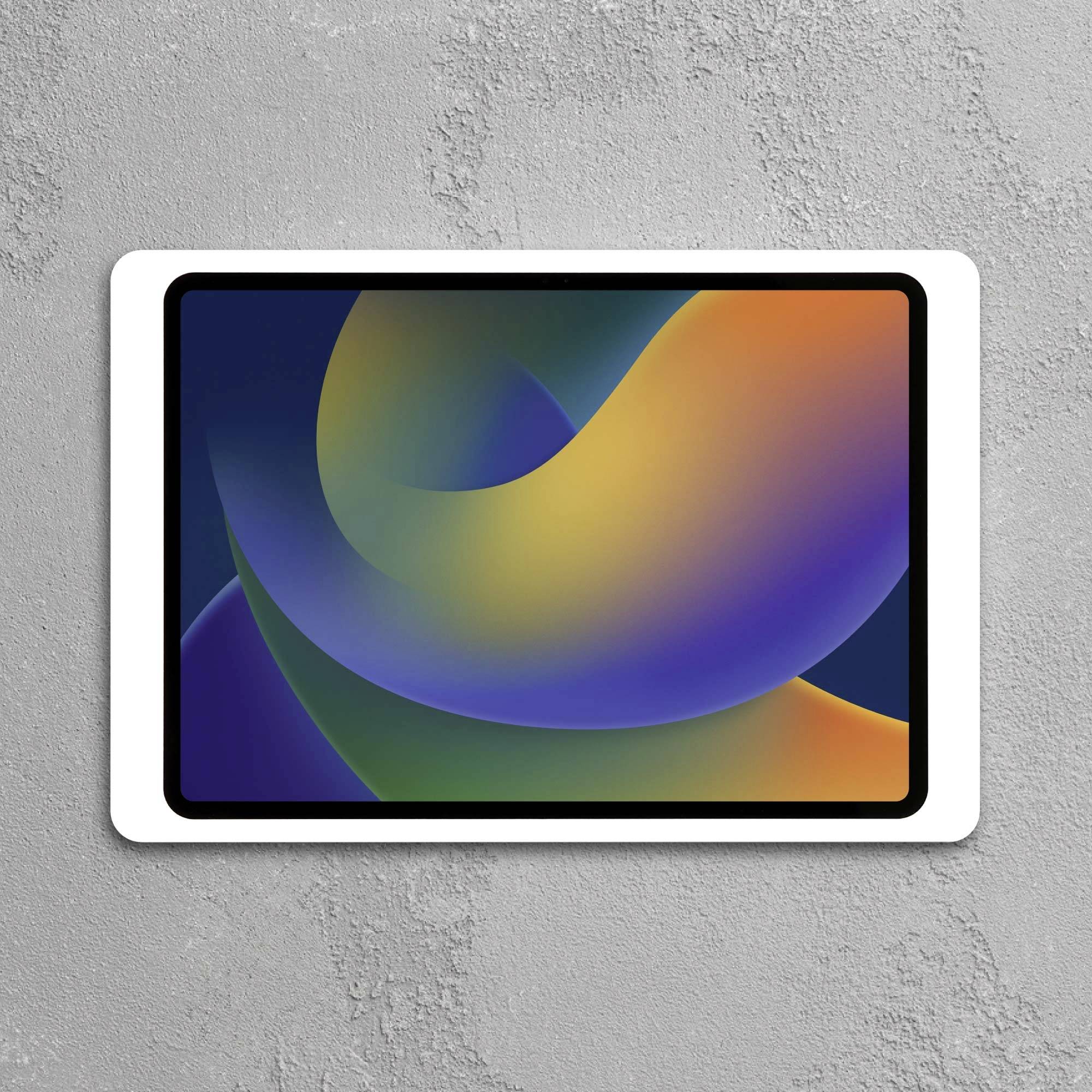 Tablet s barevným abstraktním uměním na obrazovce, umístěný na šedé stěně.
