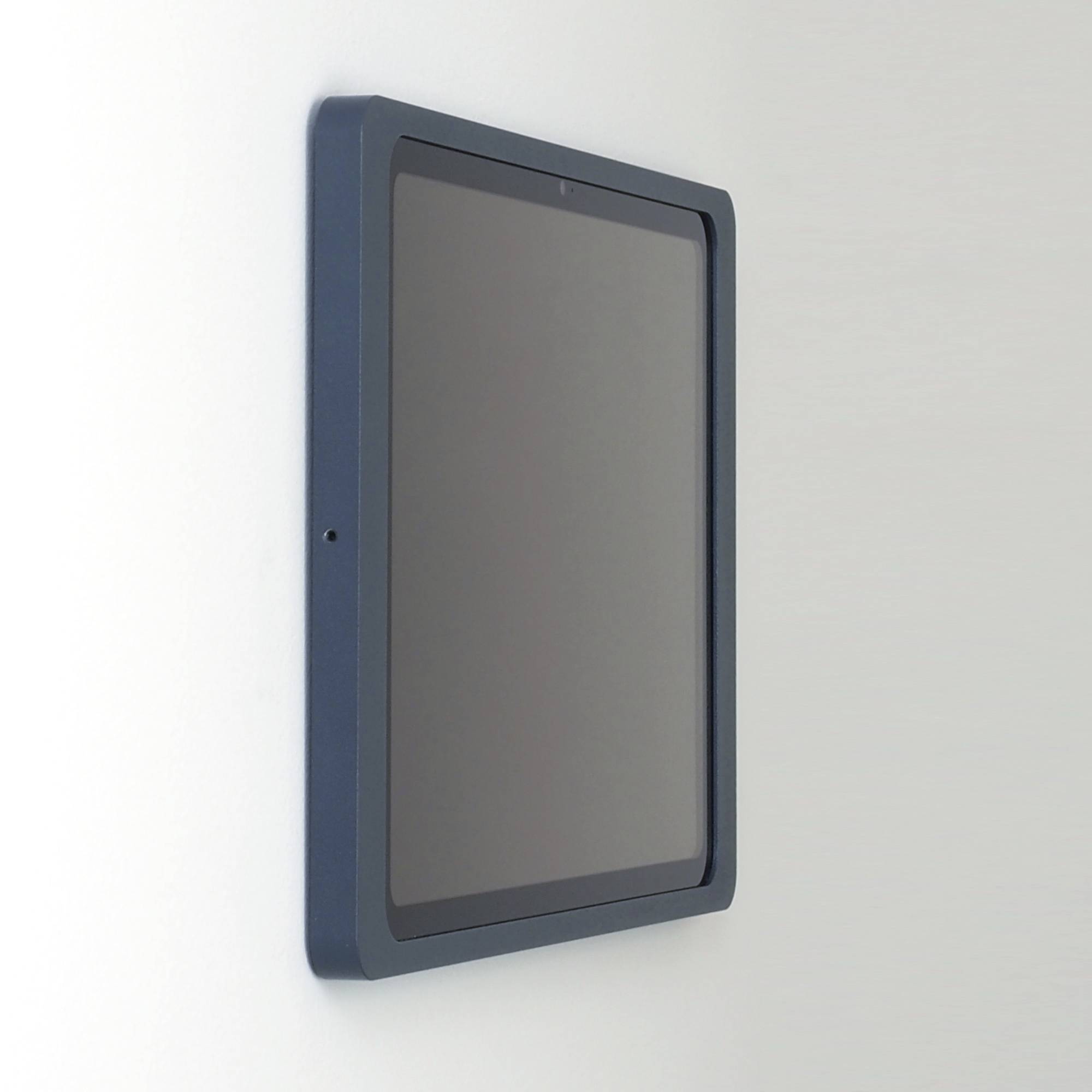 Tablet je připevněn na nástěnném držáku. Displej je vypnutý.