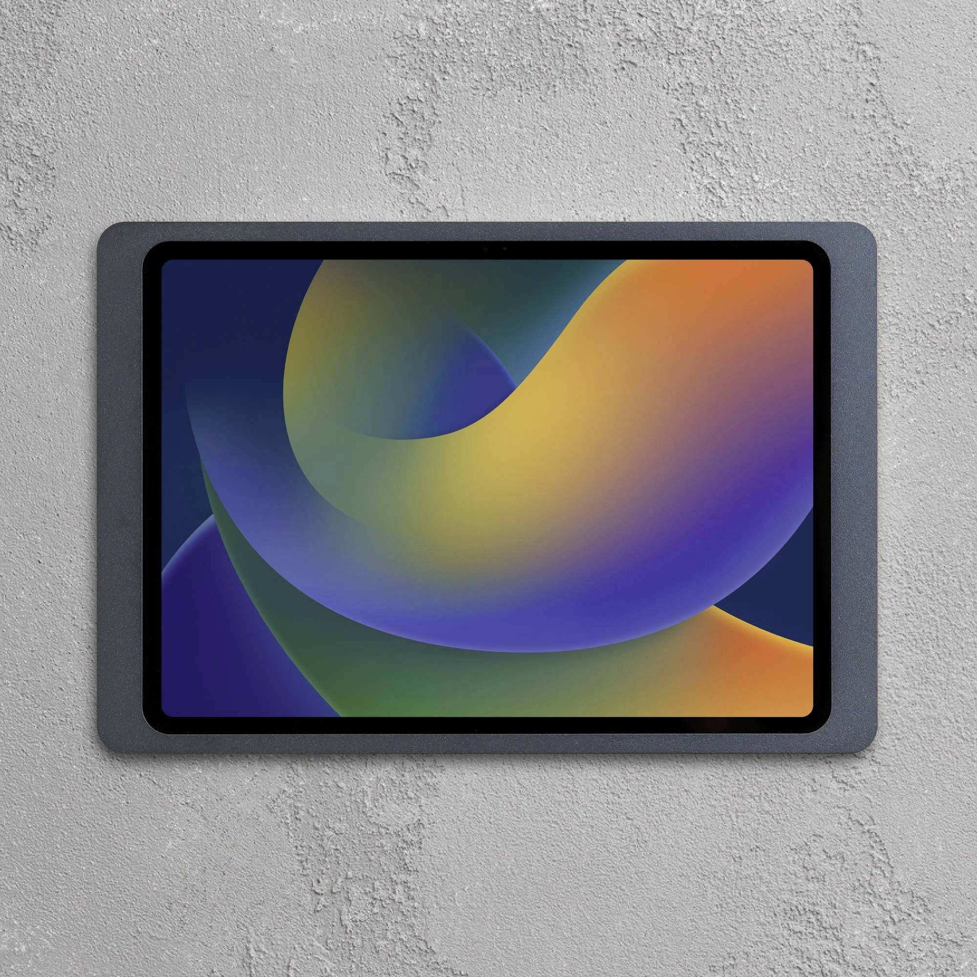 Tablet s abstraktním, barevným displejem upevněný na šedé betonové zdi.