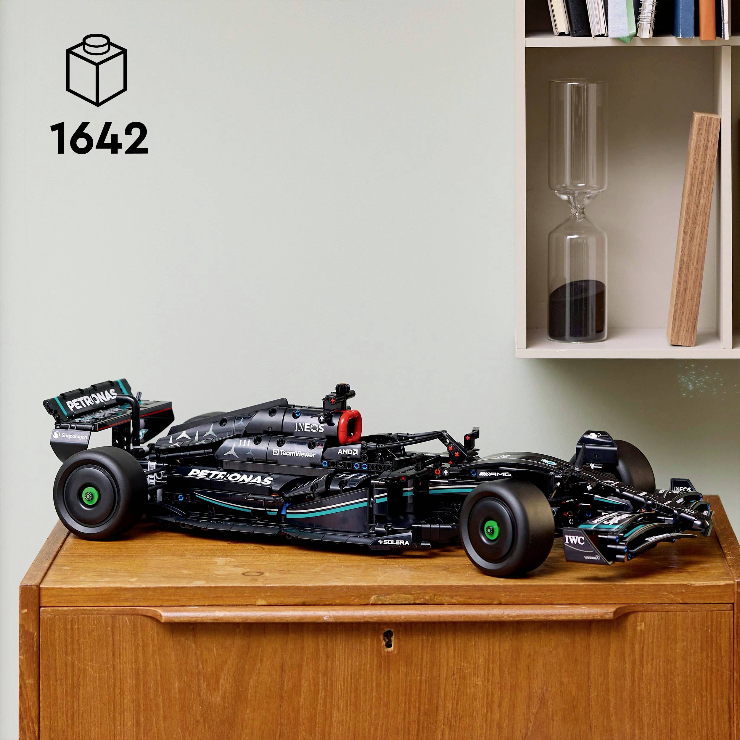 Model formule 1 na dřevěné skříni, v černé barvě s logy sponzorů, vedle police se sklem a knihami.