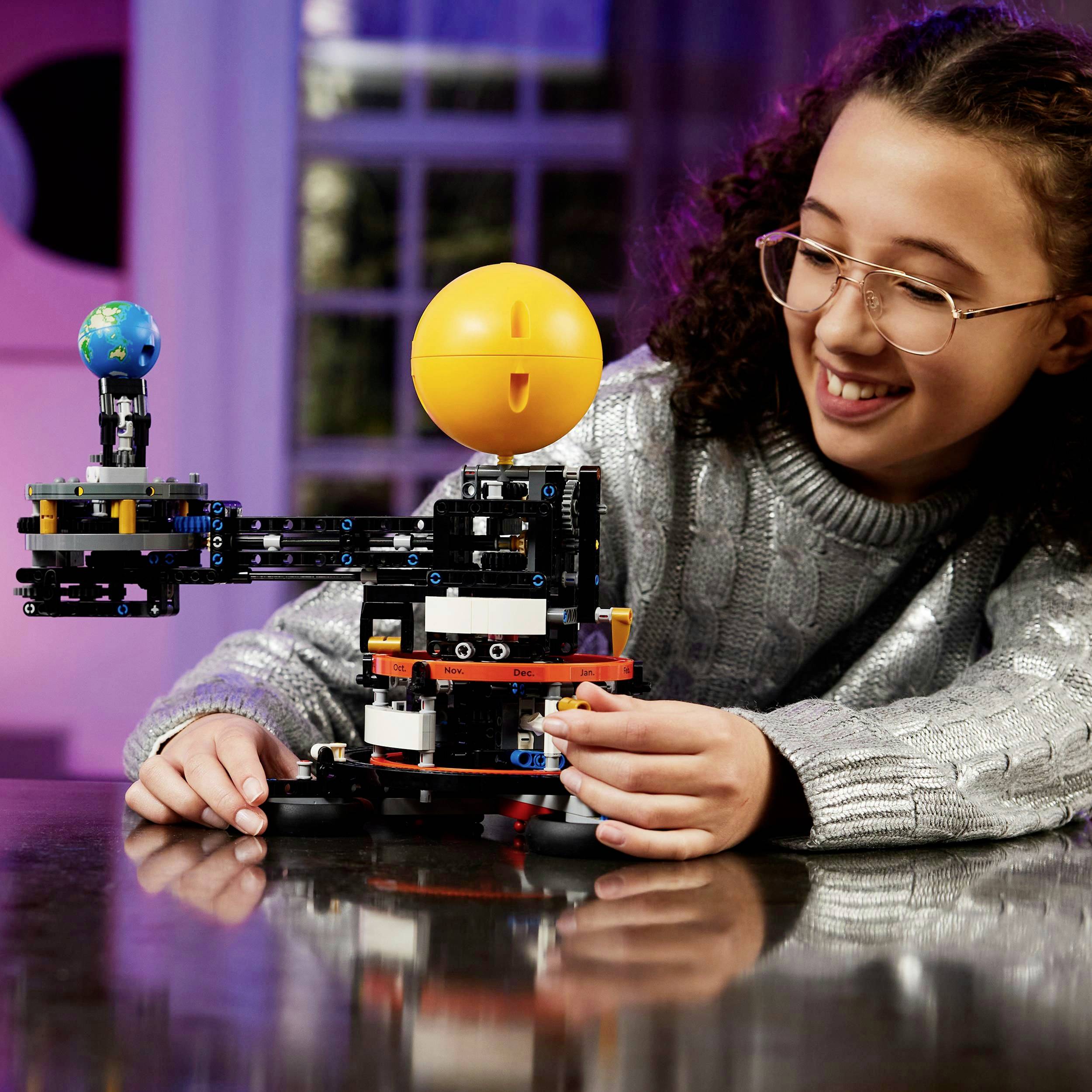 Dítě si hraje se STEM stavebnicí na stole. Stavebnice je složena z barevných stavebních bloků a zobrazuje planetární model. Dítě vypadá soustředěně a šťastně.