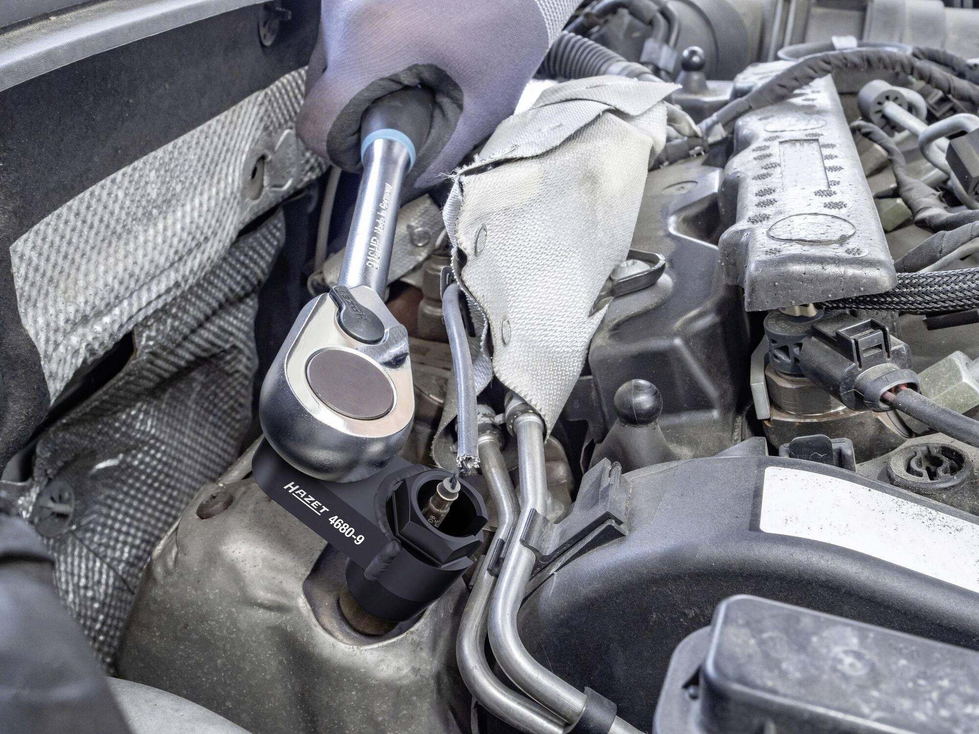Mechanik utahuje šroub momentovým klíčem v motorovém prostoru automobilu. Jsou viditelné různé součásti motoru.