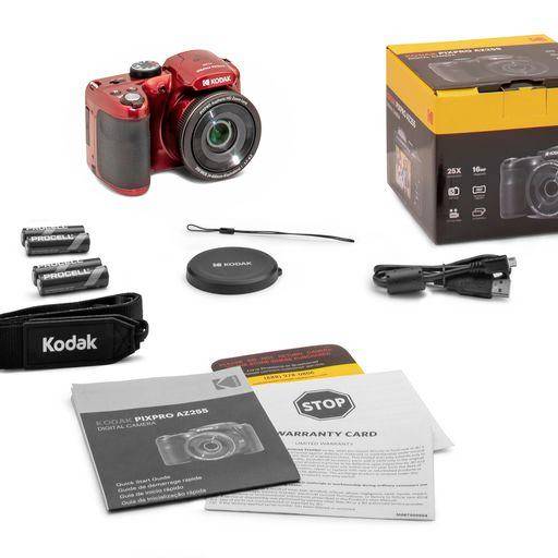 Červený digitální fotoaparát s příslušenstvím: baterie, nabíječka, krytka objektivu, řemínek na fotoaparát a návod vedle obalu.