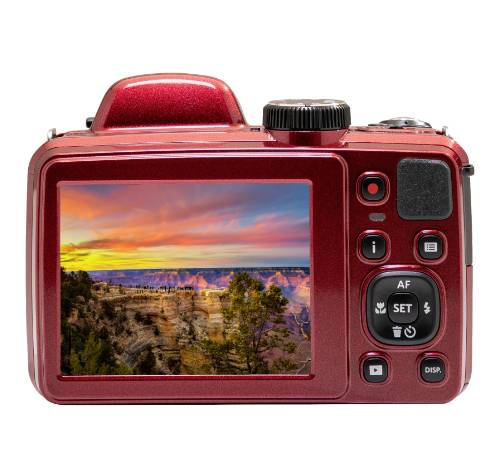 Červený digitální fotoaparát zobrazuje na displeji snímek barevného západu slunce nad kaňonem s stromy v popředí.