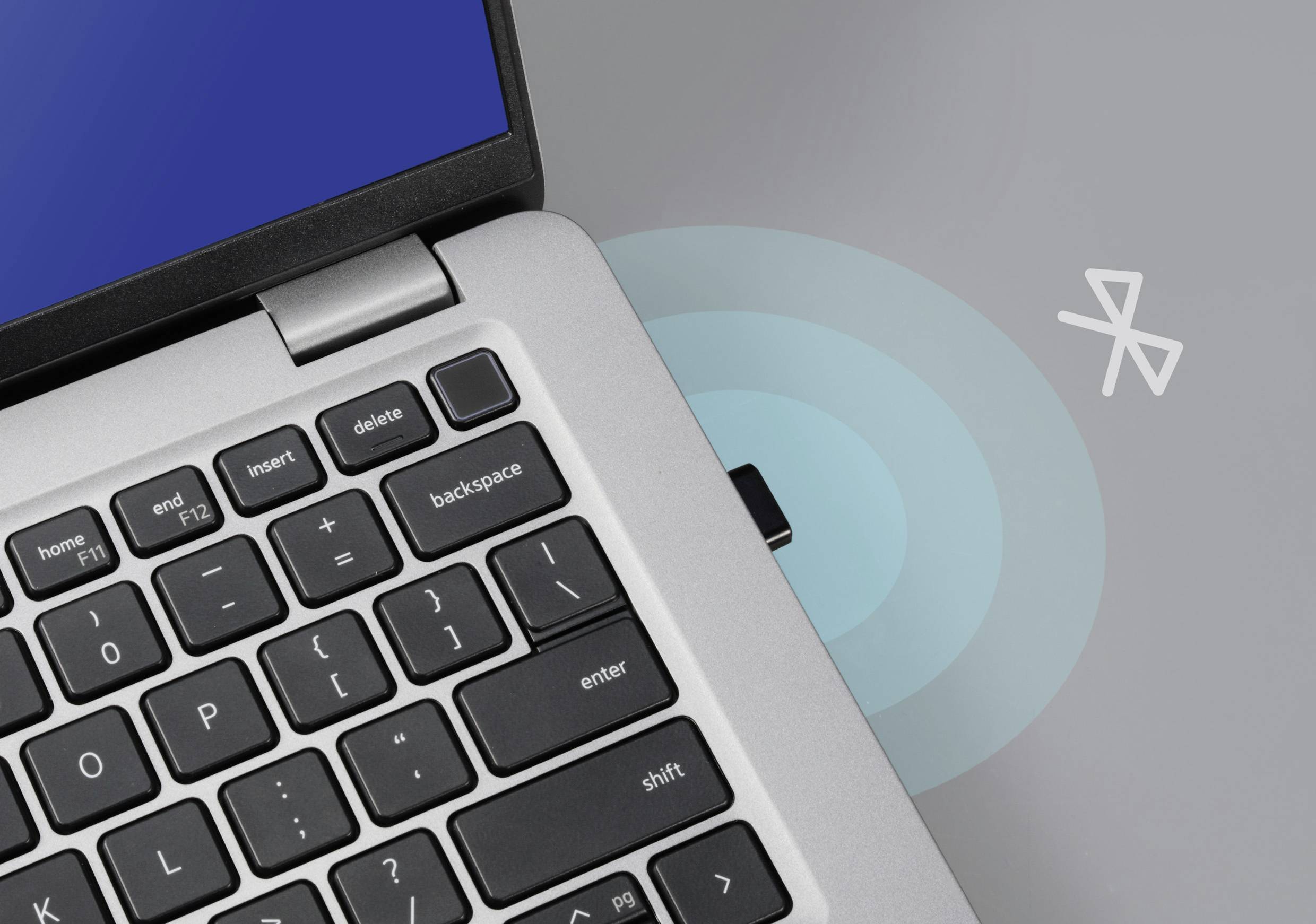 Notebook s bluetooth symbolem, zobrazující bezdrátové připojení; zaměření na klávesnici a aktivovaný bluetooth modul.