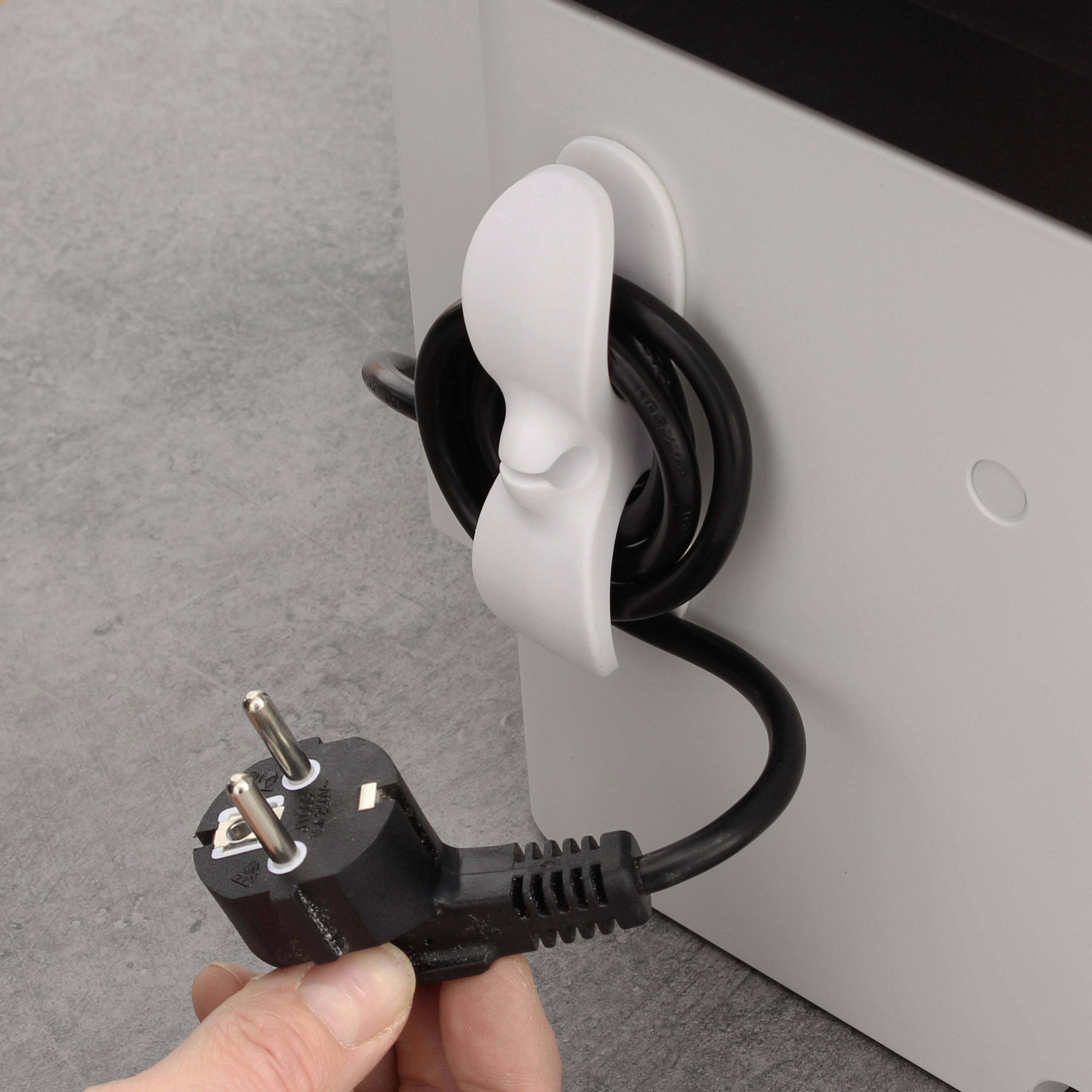 Jedna ruka drží zasunutou černou zástrčku. Bílý kabel je namotán kolem háčku na elektrickém přístroji.
