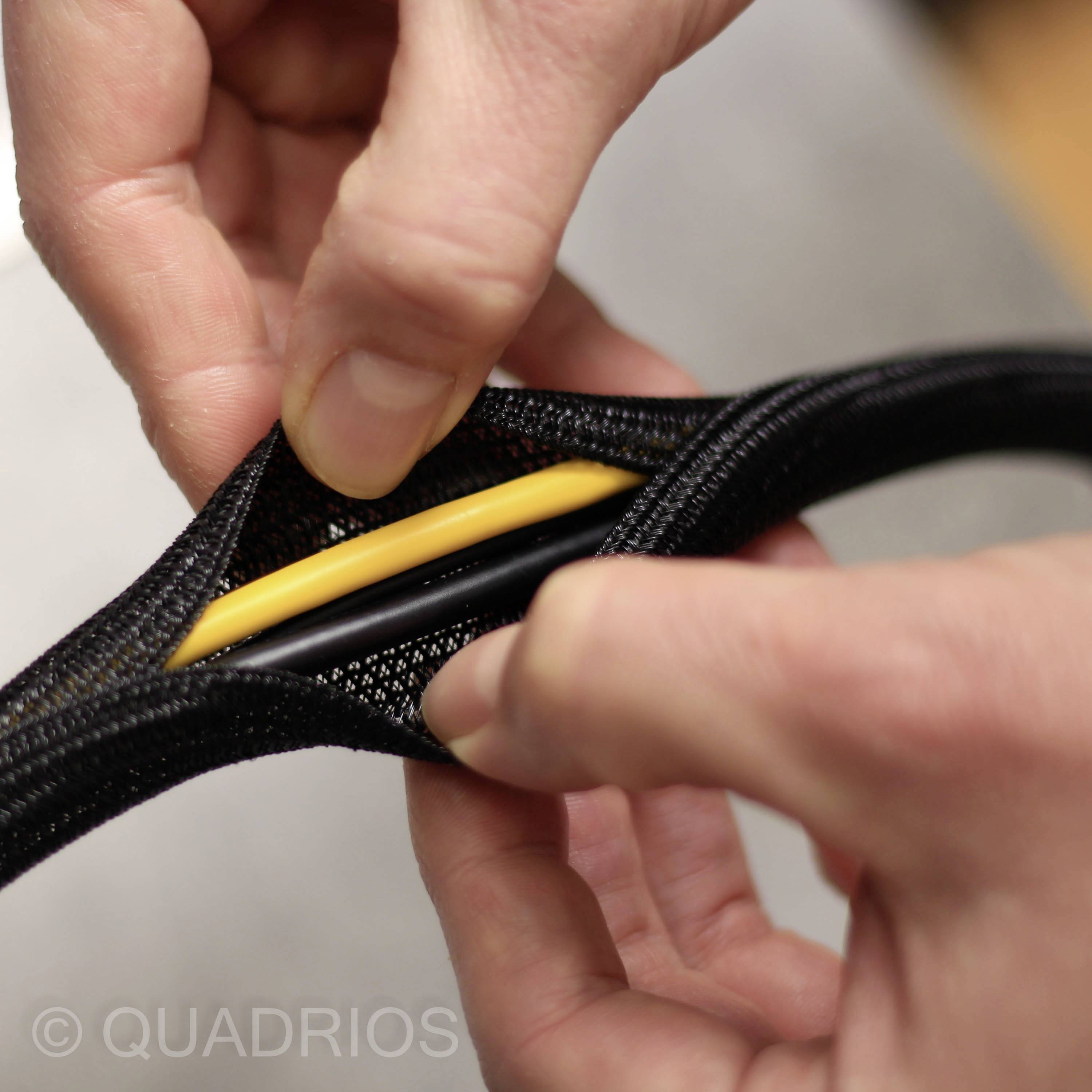 Dvě ruce roztahují černý kabelový obal, aby odhalily žlutý a černý kabel uvnitř.