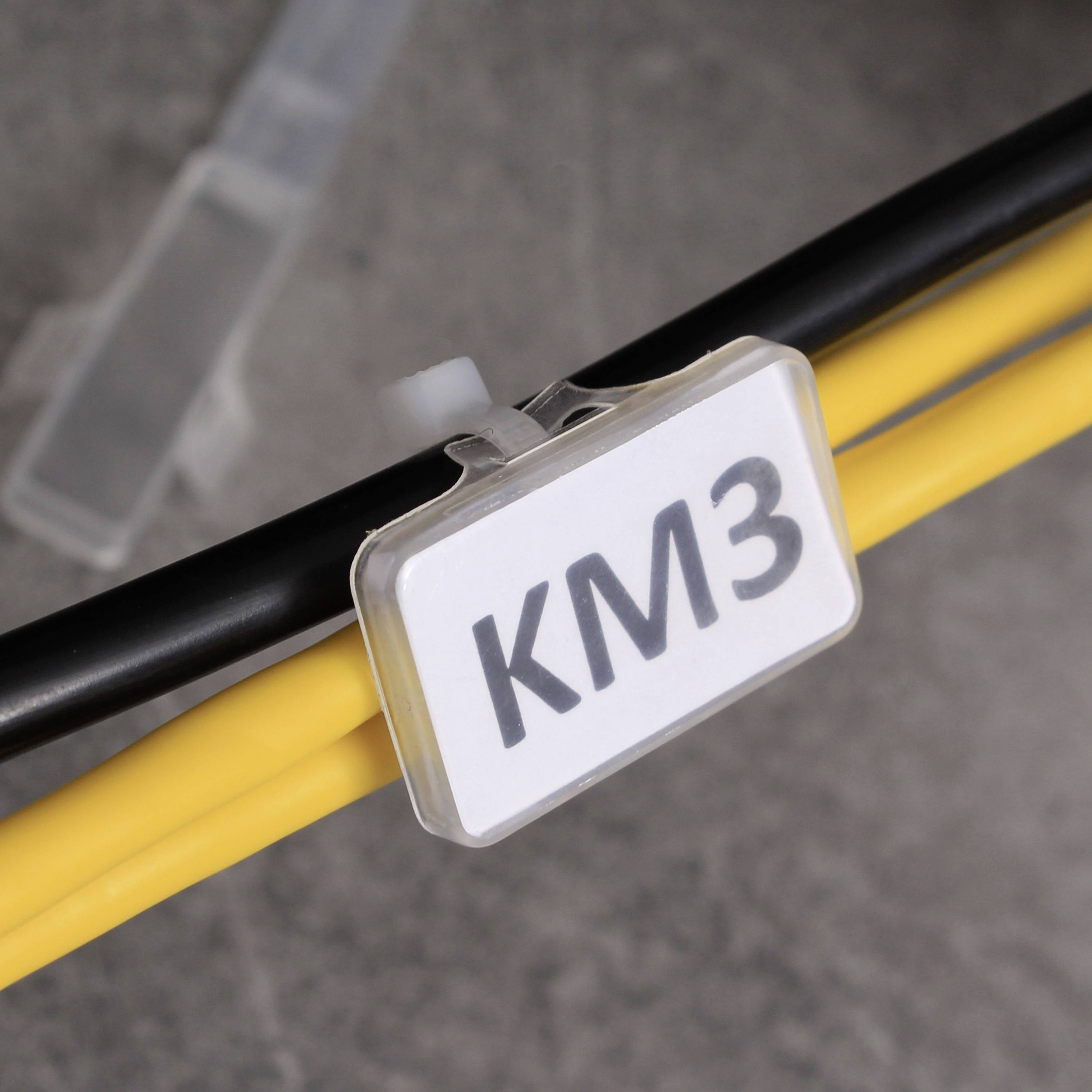 Štítek s nápisem 'KM3' upevněný na žlutém kabelu, který je doprovázen černým kabelem.