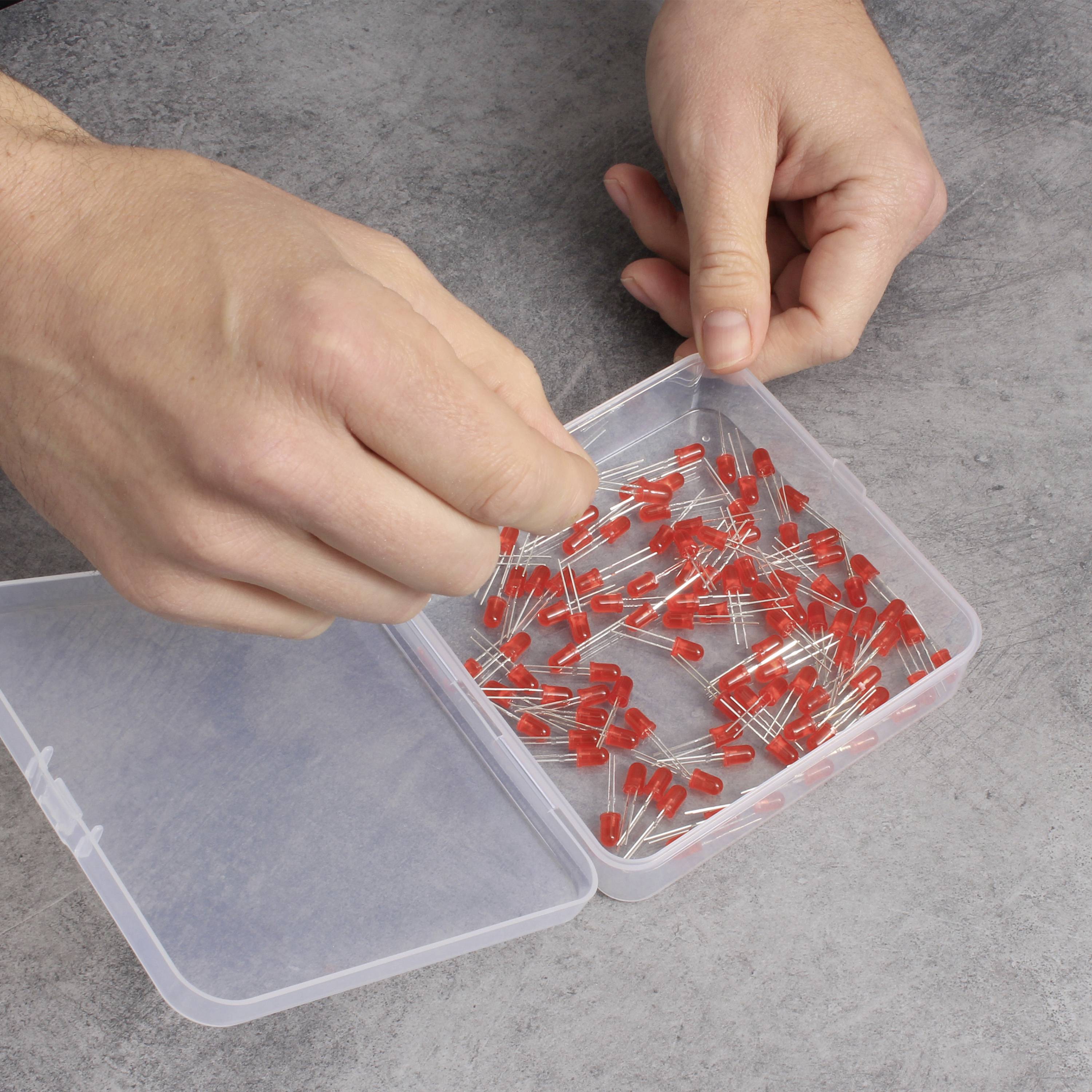 Osoba drží krabici plnou červených izolátorů elektrického vedení na betonovém povrchu.