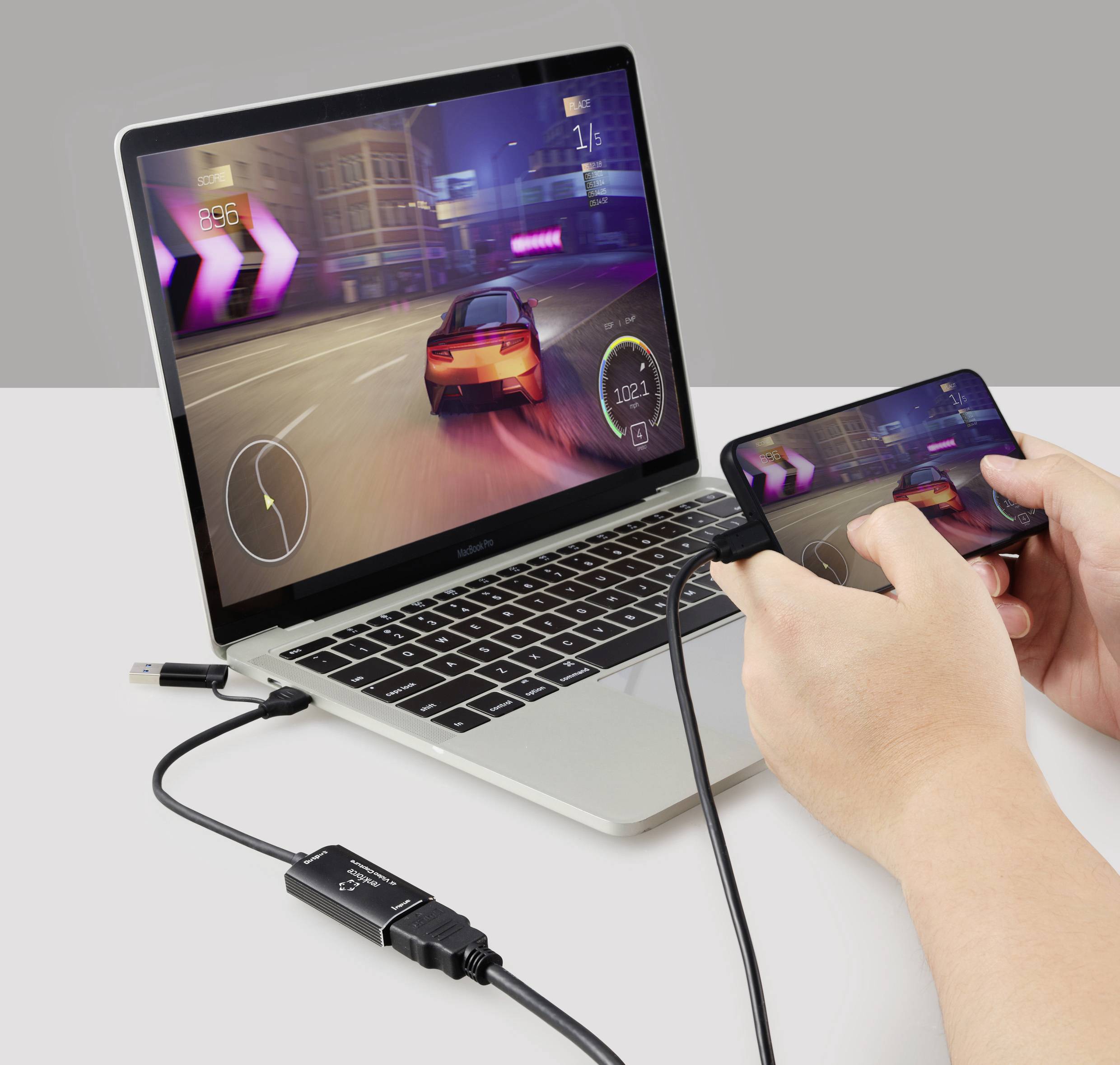 Osoba hraje závodní hru na smartphonu, který je připojen kabelem k laptopu. Laptop zobrazuje stejnou hru.