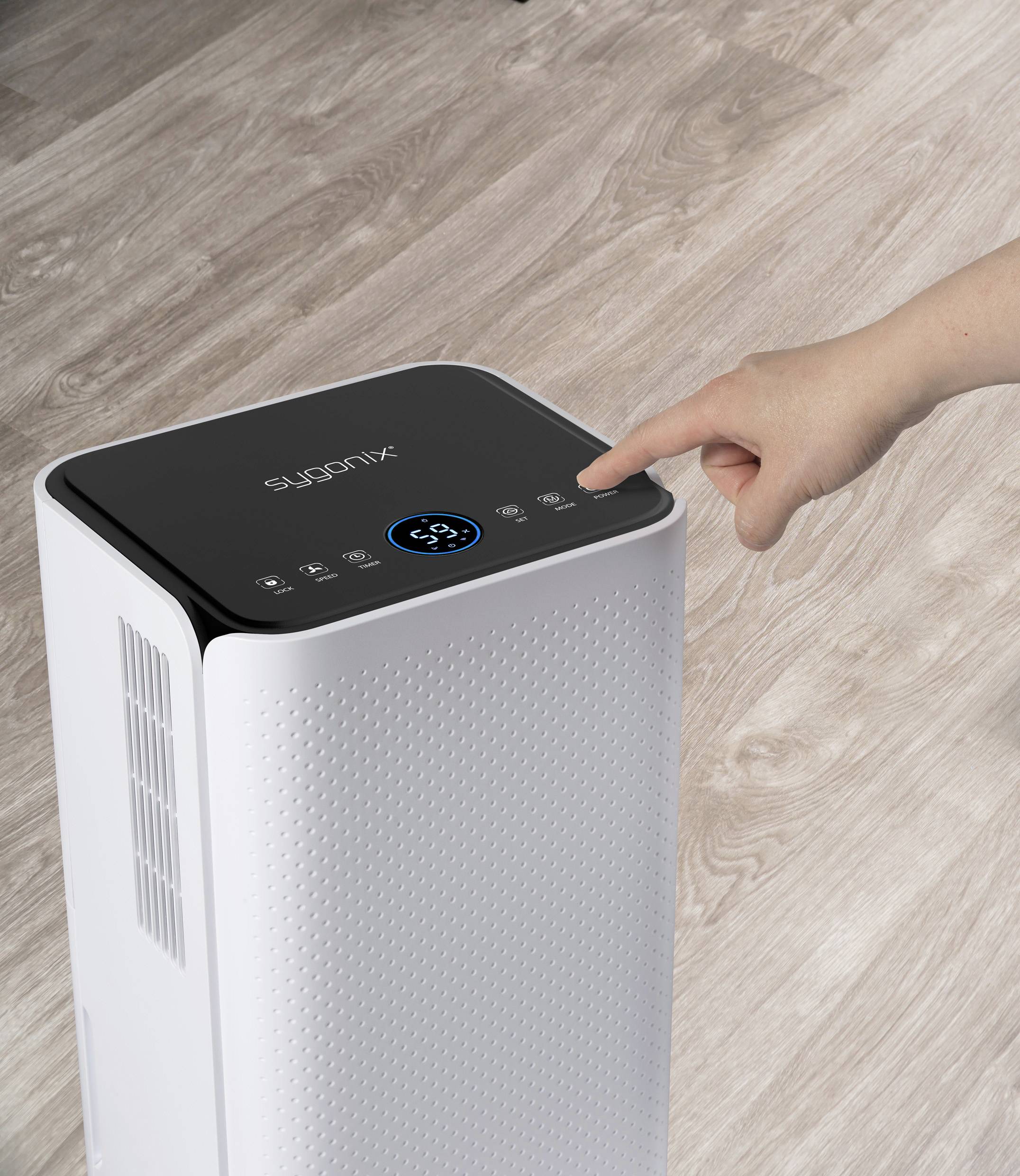 Ruční ovládání čističky vzduchu na dřevěné podlaze. Digitální displej ukazuje číslo 58. Čistička vzduchu má moderní, bílý design.
