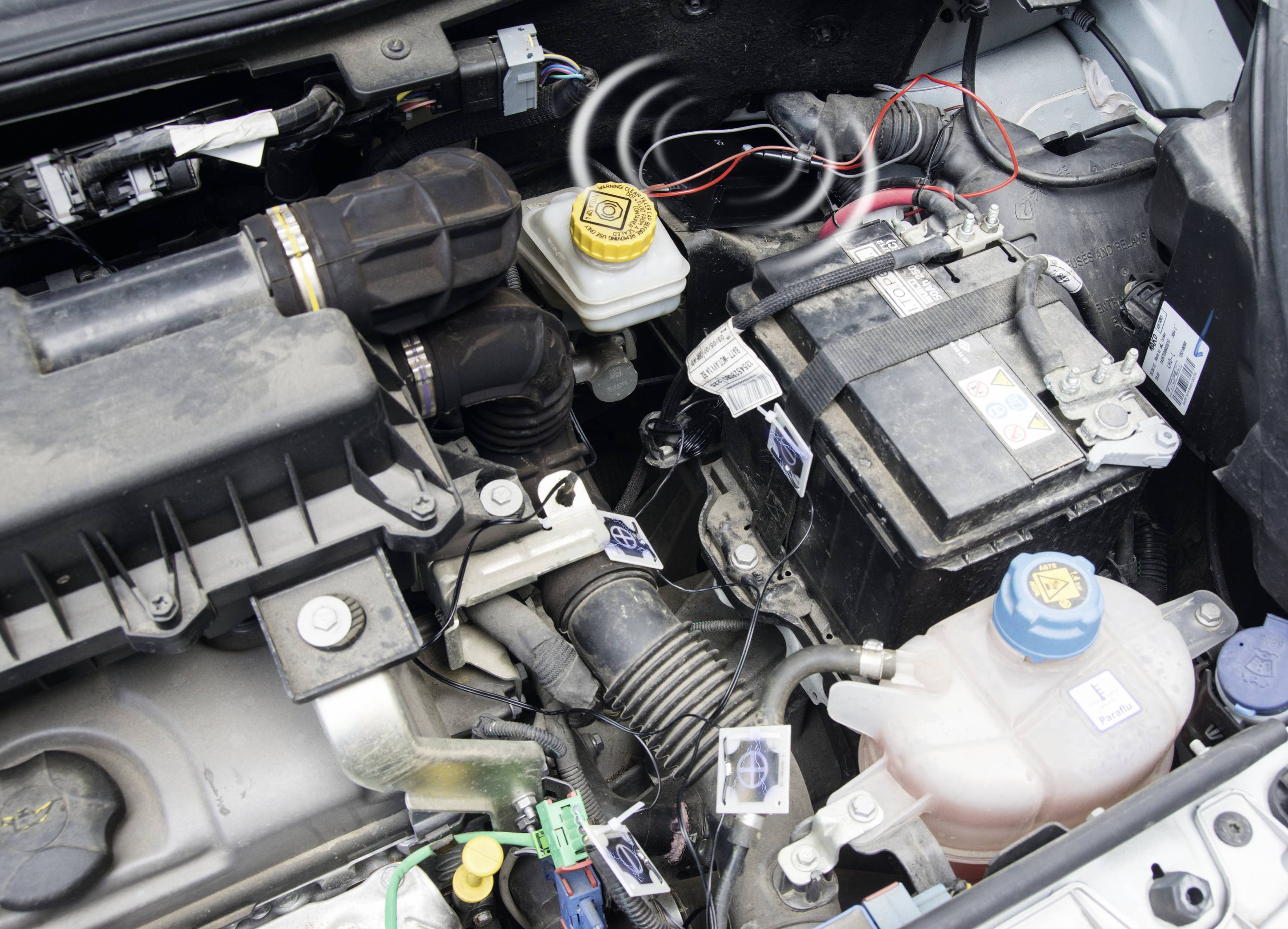 Motorový prostor automobilu s baterií, nádobkou chladicí kapaliny, krytem vzduchového filtru a nádobkou brzdové kapaliny. Viditelné elektrické kabely.
