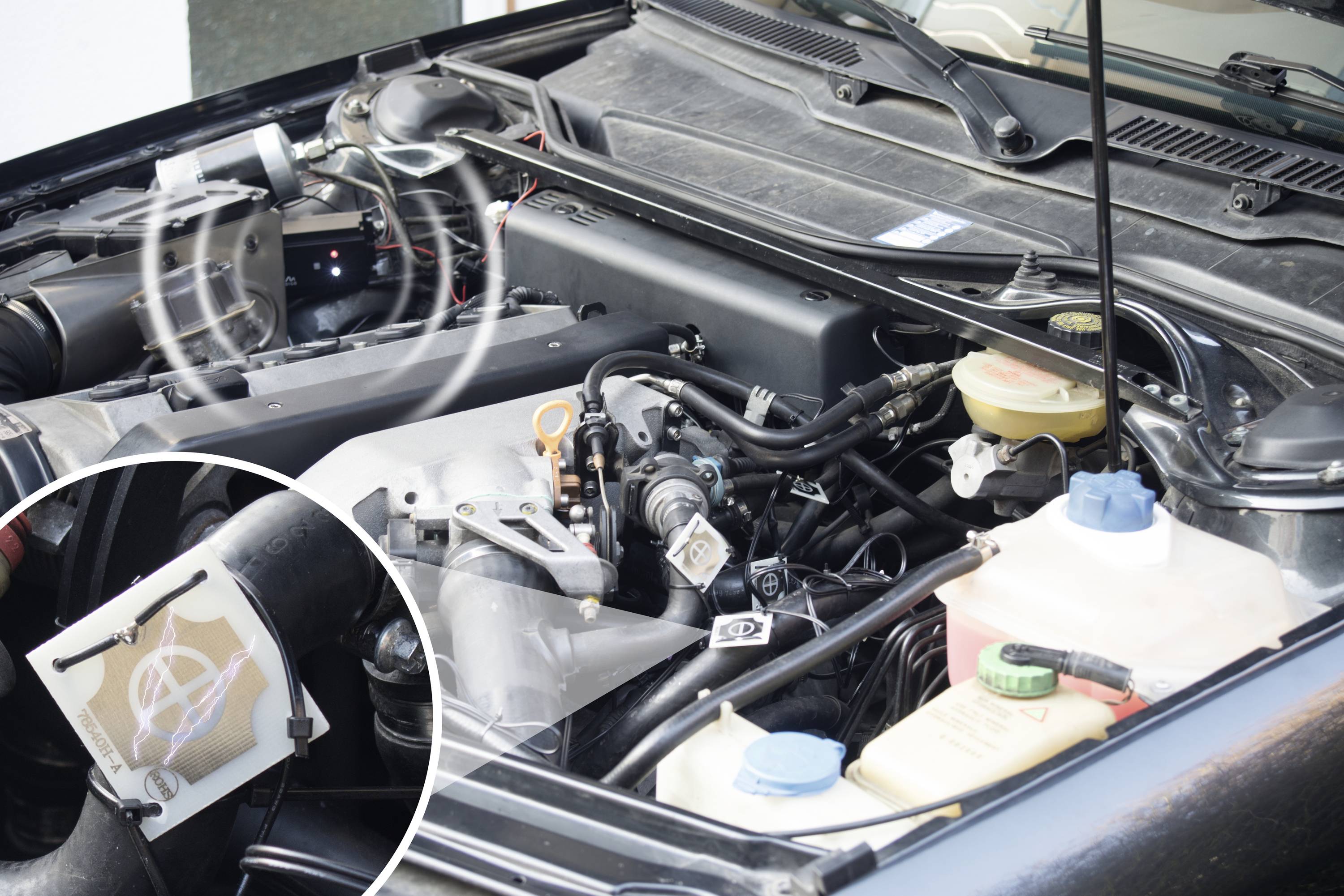 Otevřený chladič automobilu s viditelnými hadicemi a nádobkami na chladicí kapalinu. Zvětšený výřez ukazuje mřížku chladiče.