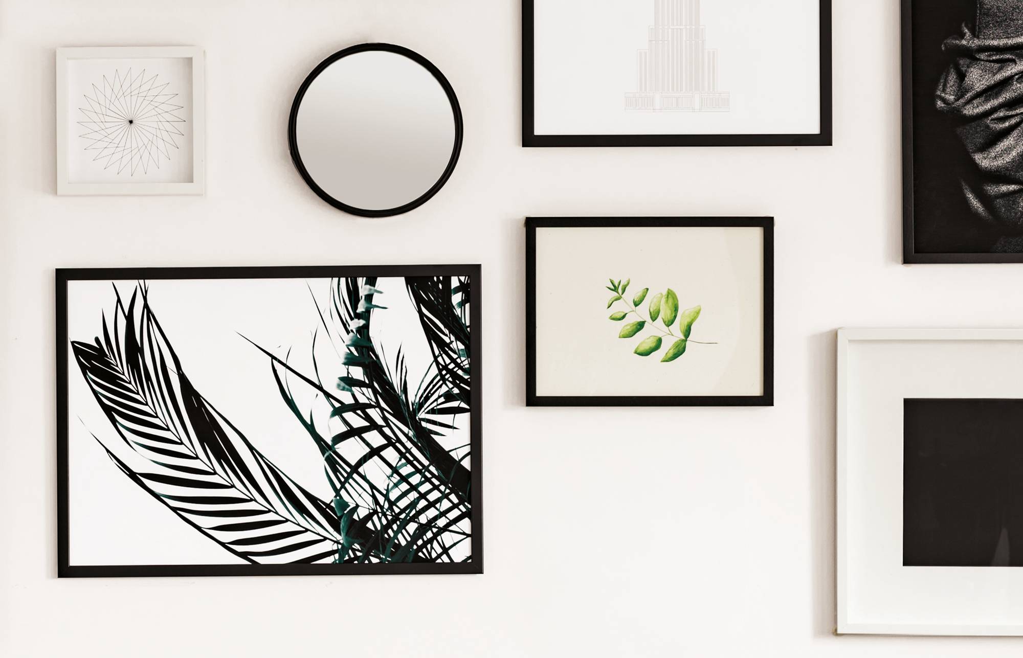 Galerie na zdi s rámovanými uměleckými tisky a zrcadly, včetně botanických ilustrací listů a abstraktních černo-bílých vzorů na bílé stěně.