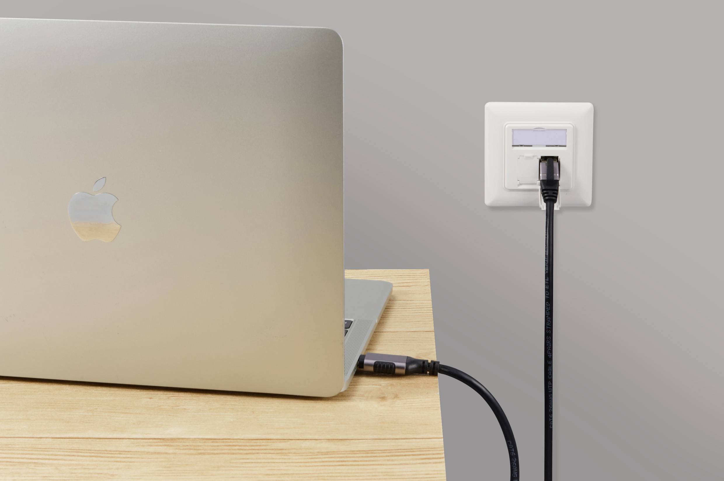 'Stříbrný laptop na dřevěném stole je připojen černým kabelem do elektrické zásuvky.'