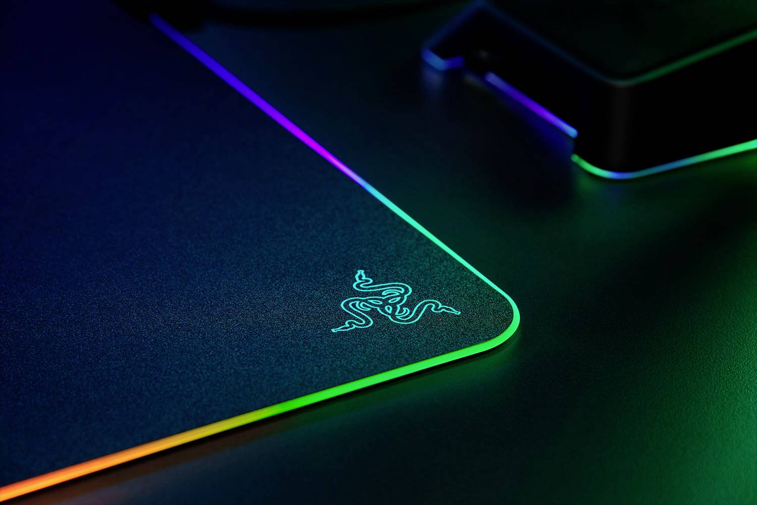 Herní podložka pod myš s osvětleným RGB okrajem a podsvíceným logem v tmavém prostředí.