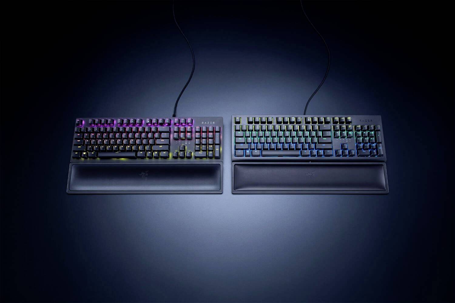 Dvě herní klávesnice na tmavém pozadí, osvětlené barevnými RGB světly, s opěrkami zápěstí, položené vedle sebe.