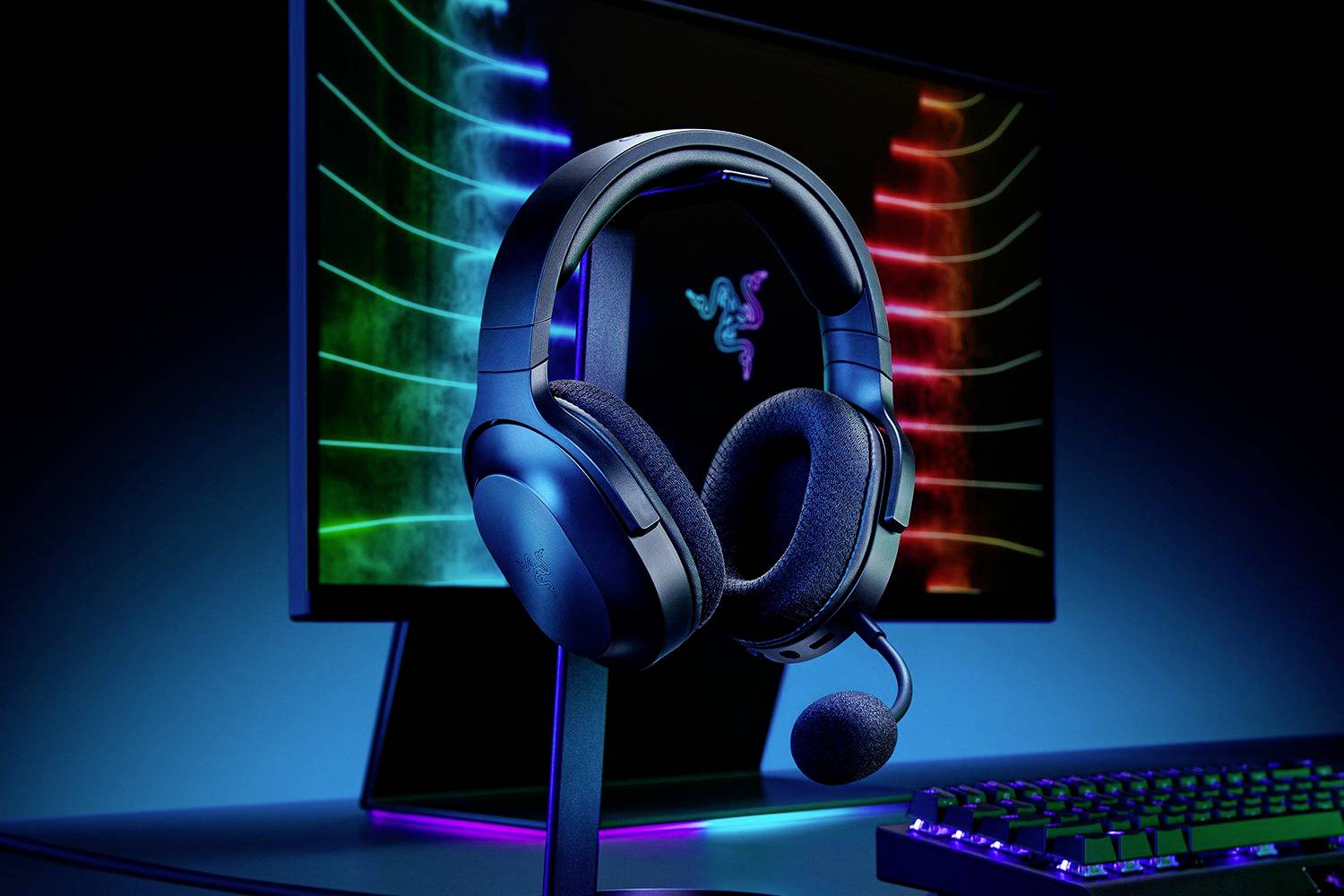 Herní headset s mikrofonem stojí na stojánku před monitorem s pulzujícími barevnými světly. Klávesnice je viditelná v zorném poli.