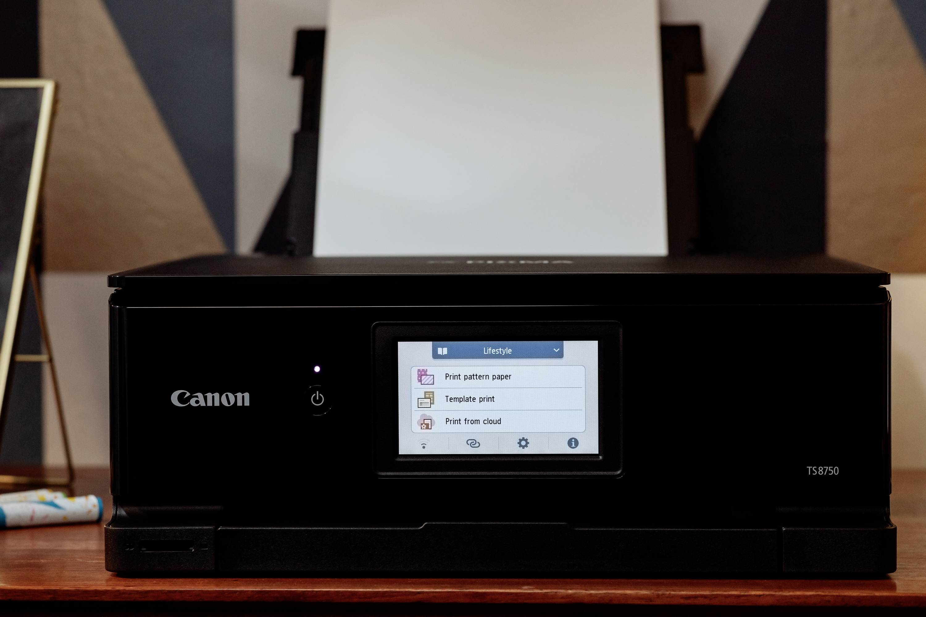 Tiskárna Canon stojí na stole, displej zobrazuje 'Tisk vzorovaného papíru', 'Tisk šablony' a 'Tisk z cloudu'.