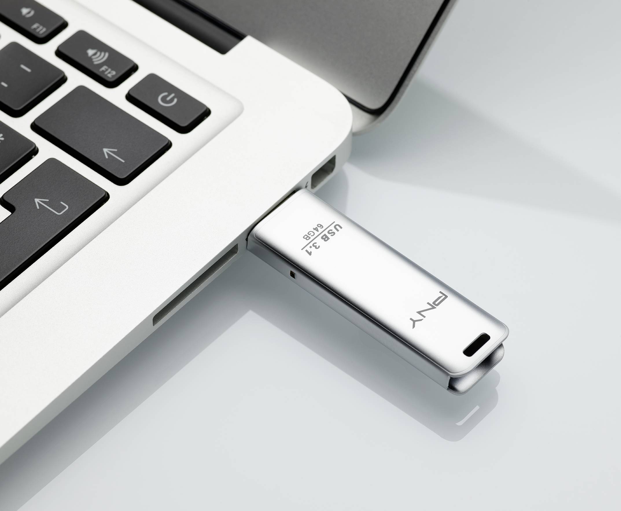 Notebook s připojeným stříbrným USB flash diskem označeným "USB 3.1" leží na hladkém povrchu.