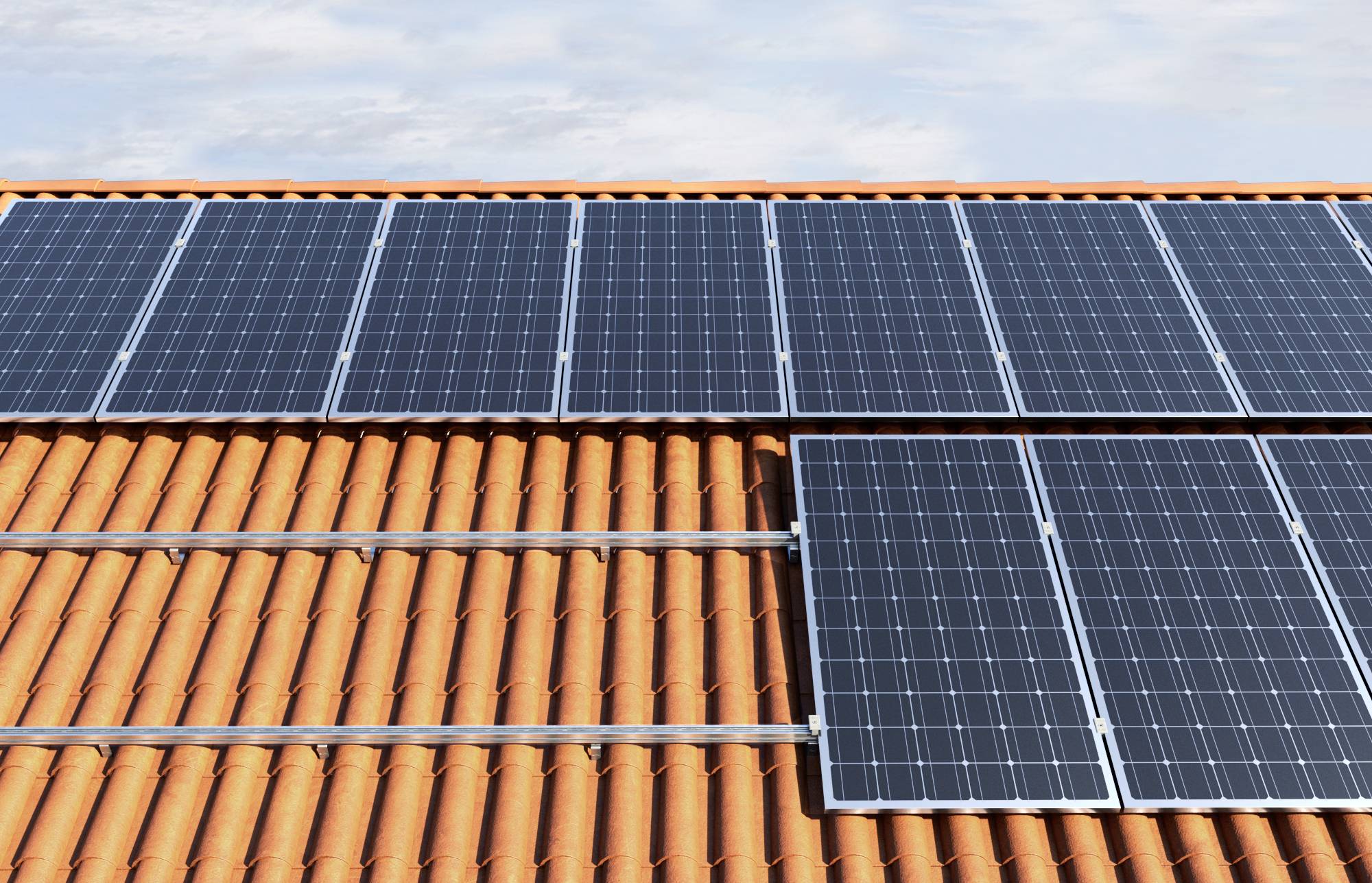 Řada solárních panelů na červené tašková střeše pod modrým nebem, které využívají sluneční energii k výrobě elektřiny.
