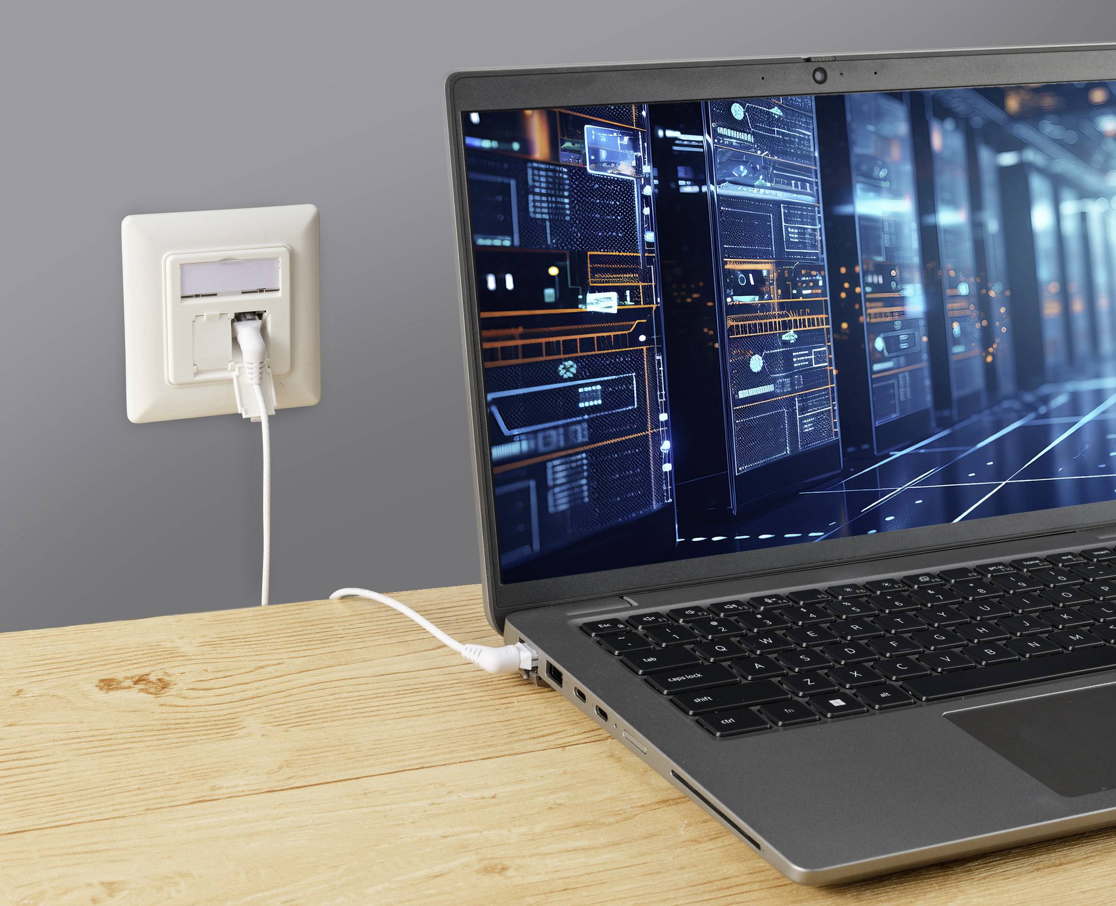 Otevřený laptop na dřevěném stole je připojen k síťovému rozhraní. Na obrazovce jsou viditelné technické diagramy.